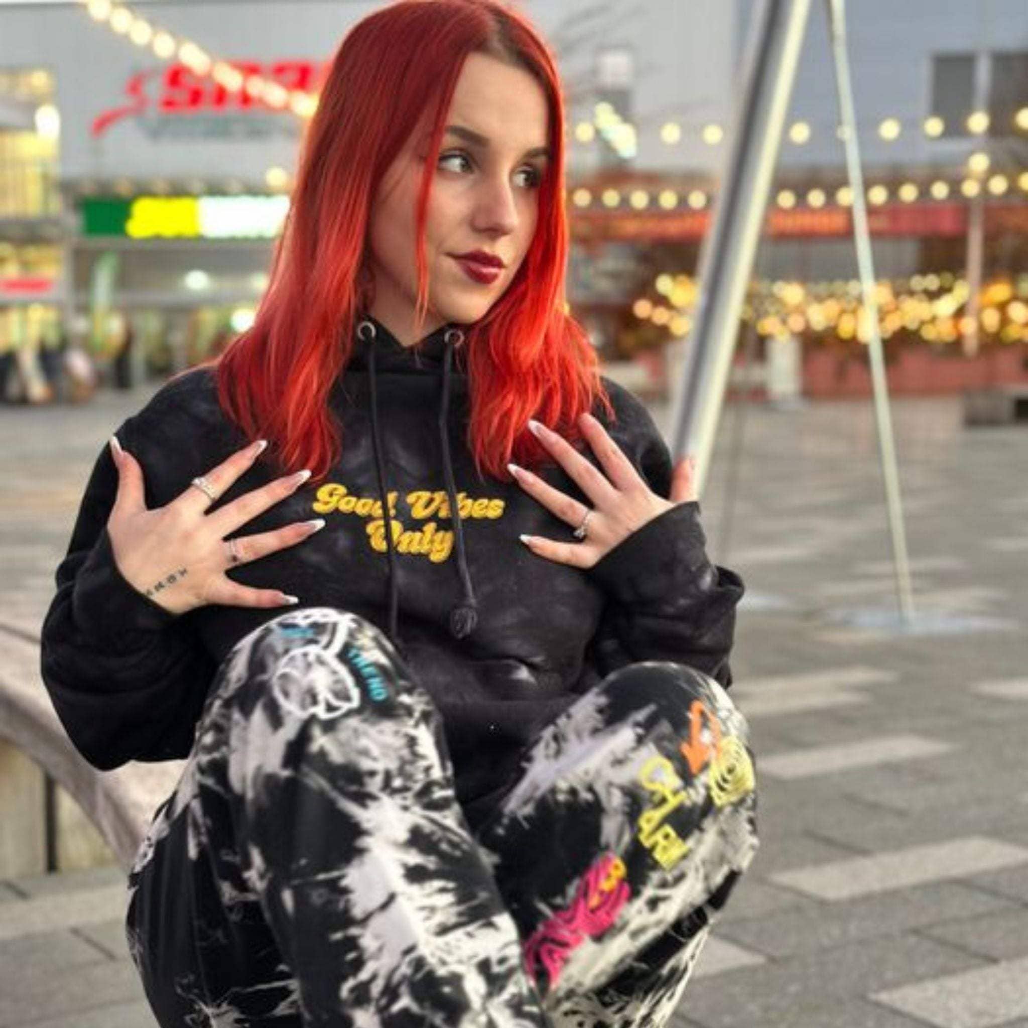 Black tie-dye hoodie with yellow "Good Vibes Only" embroidery worn by red-haired woman outdoors