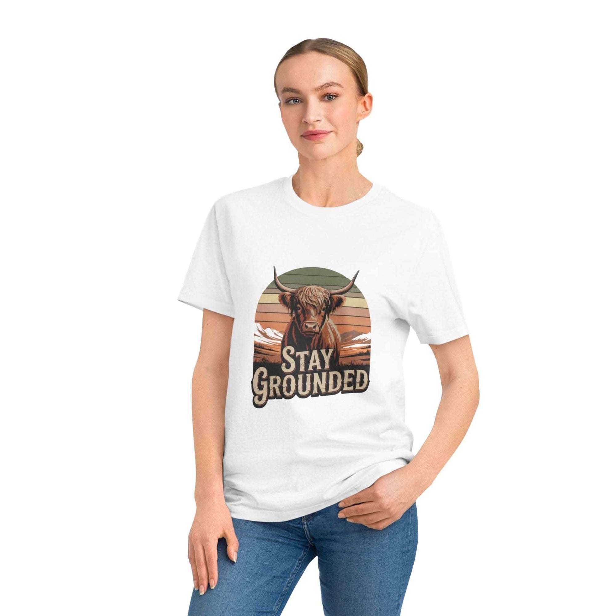 Person wearing a white t-shirt with a graphic of a cow and 'Stay Grounded' text on a plain background