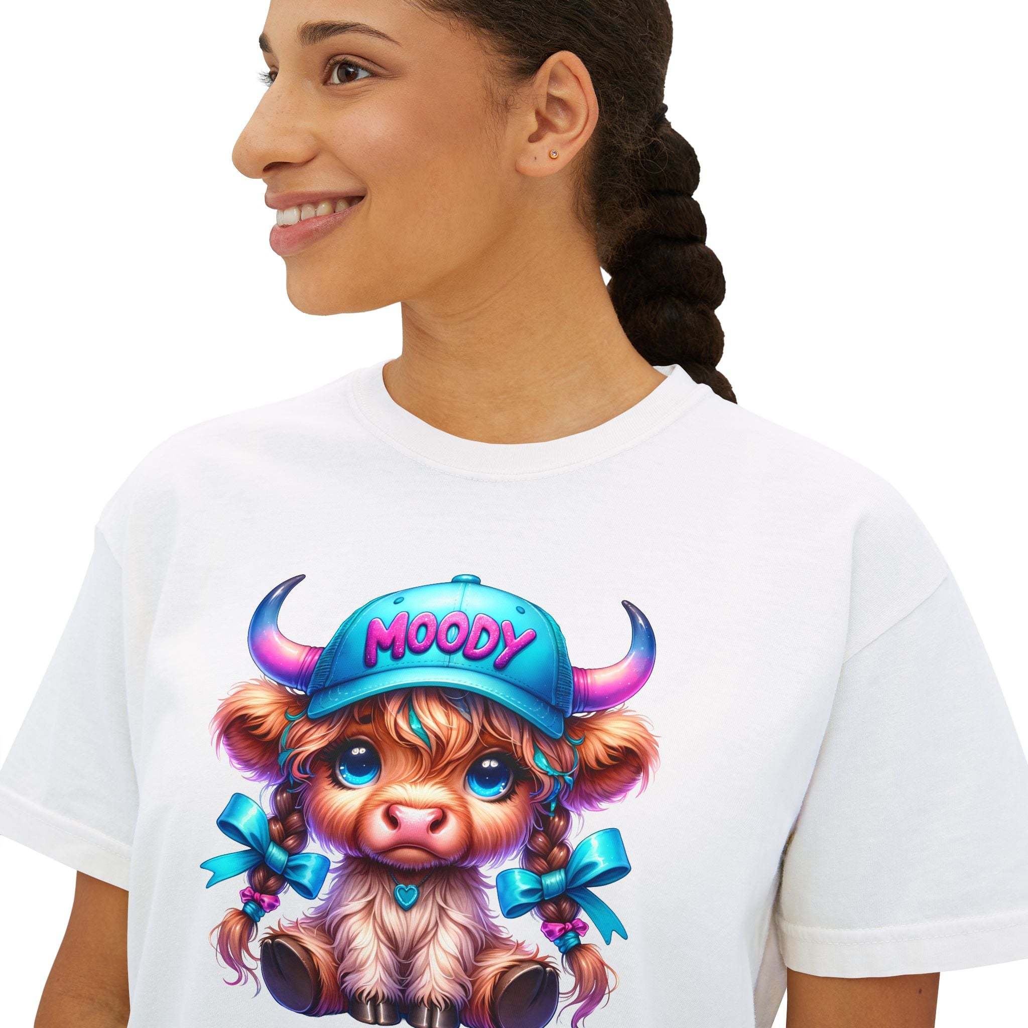 Woman wearing white boxy tee with moody girl highland cow graphic and blue cap