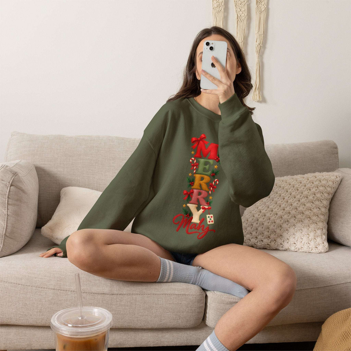 Female model taking a selfie and wearing a Military green Merry Mahj Christmas mahjong sweatshirt with colorful stacked lettering, red bows, candy canes, holly and a mahjong tile.