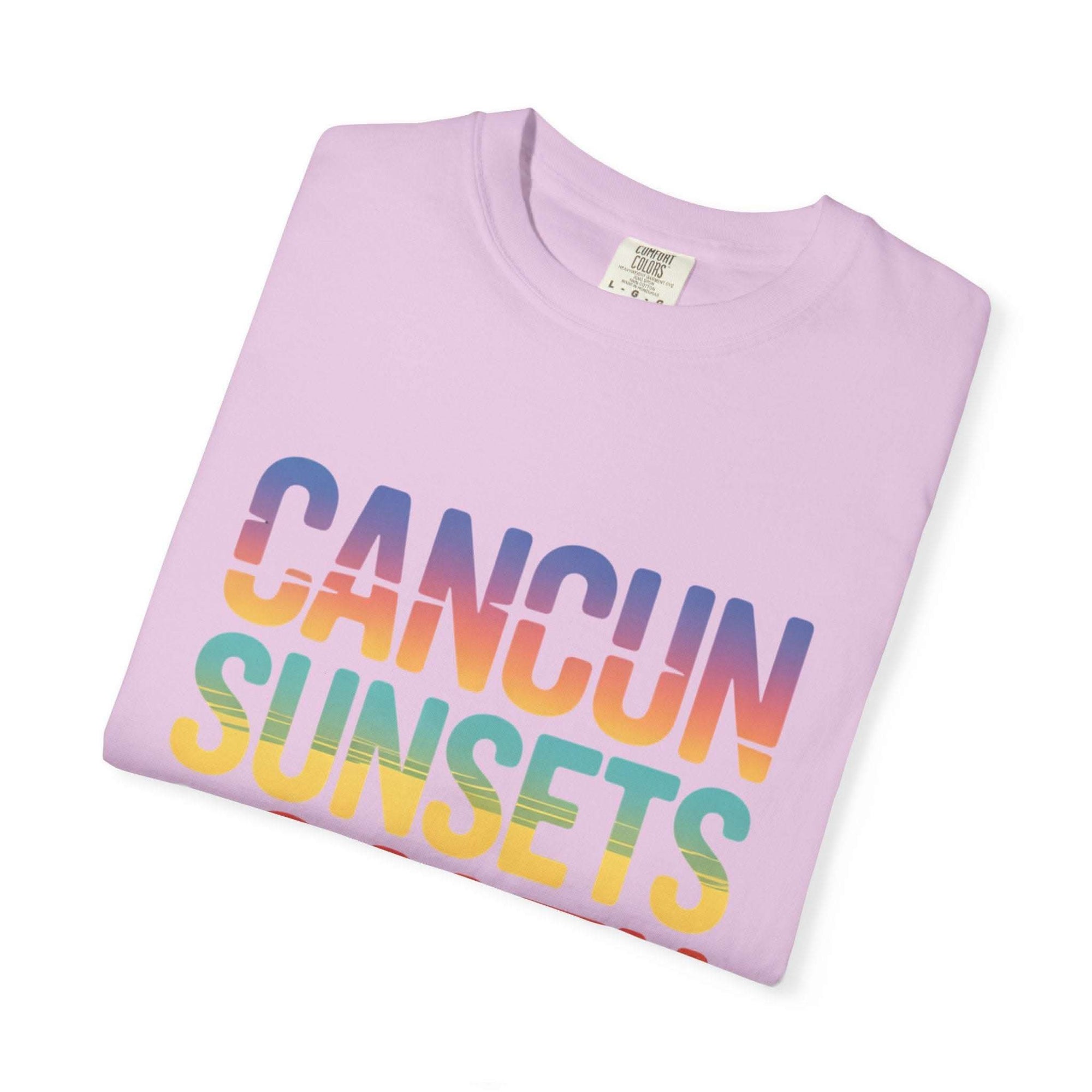 Folded pink t-shirt with 'Cancun Sunsets' text in rainbow colors on a white background