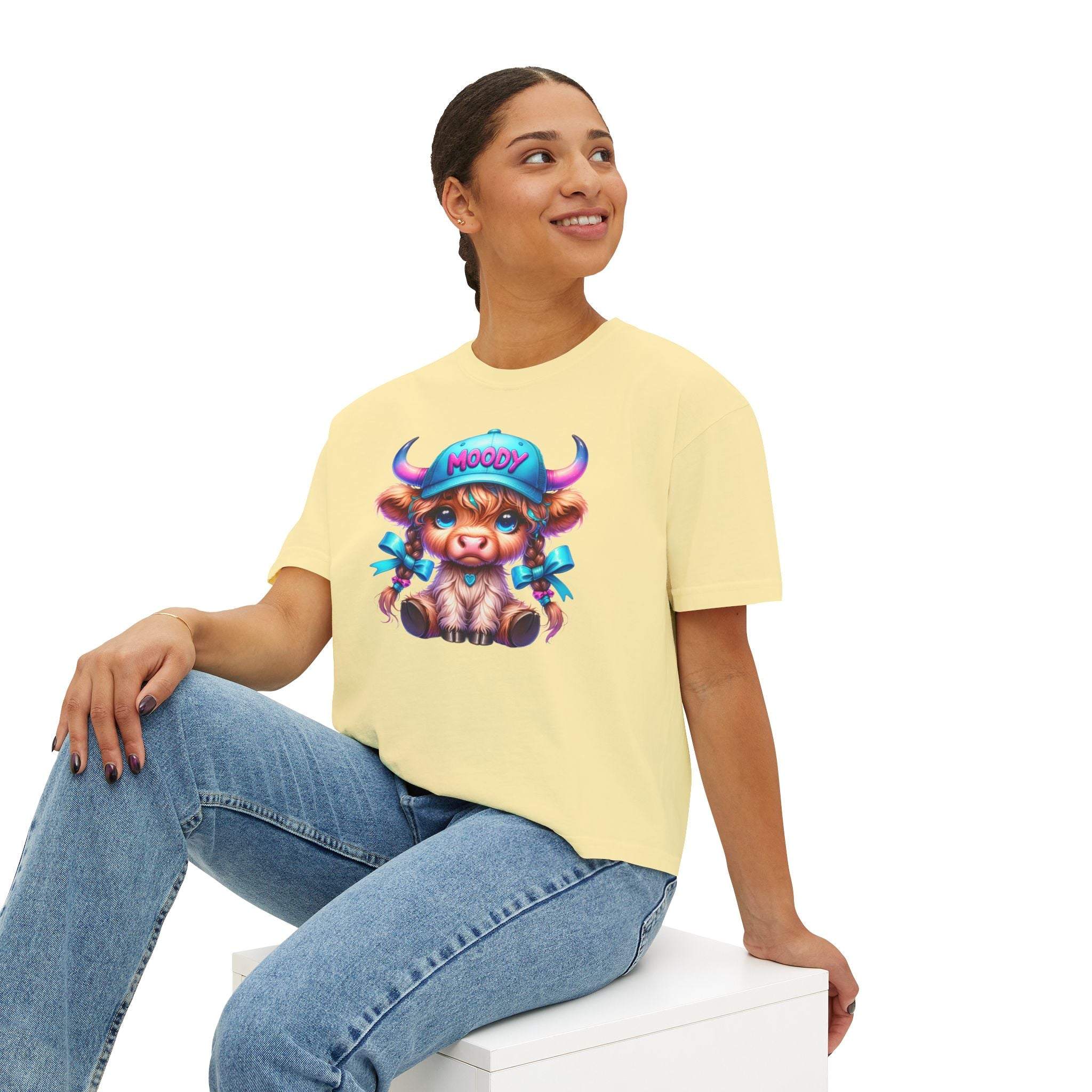 Woman wearing yellow boxy tee with moody girl highland cow graphic sitting and smiling