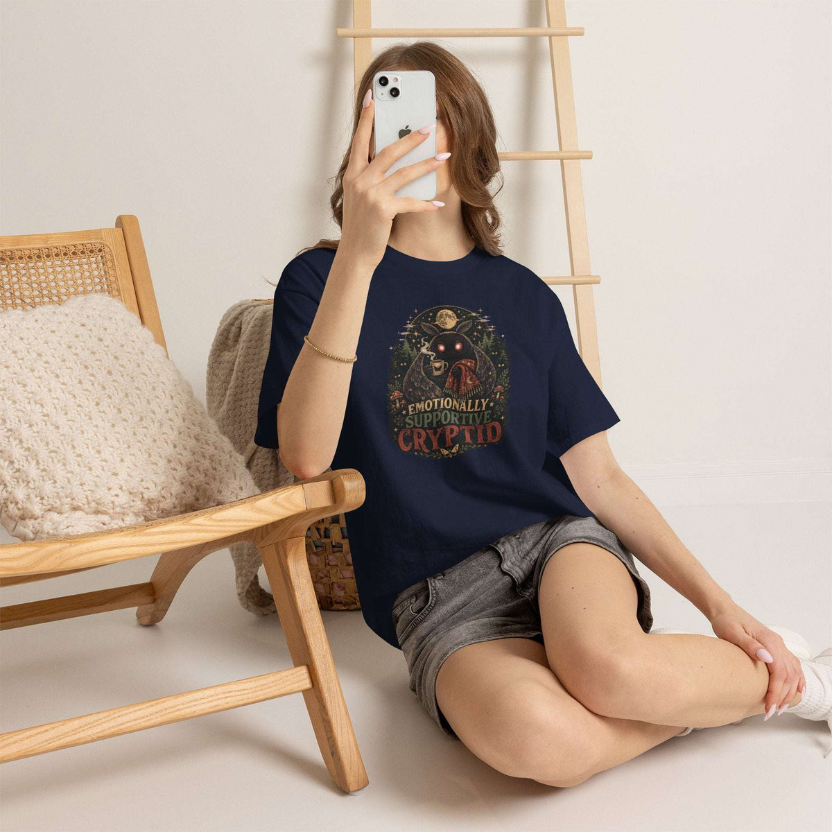 Surreal glowing-eyed mothman cryptid in cozy blanket holding mug design on cryptid tee