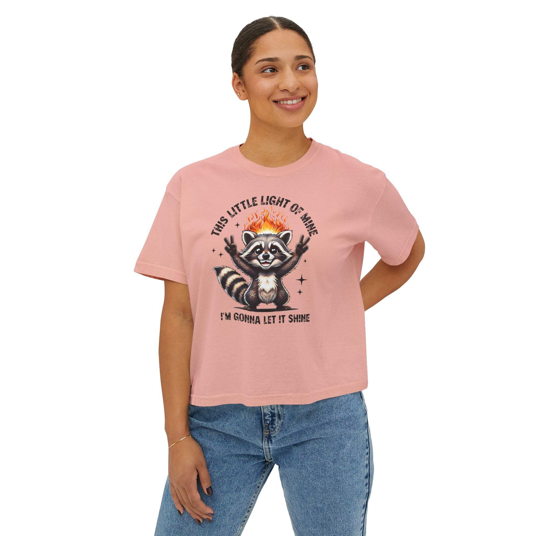 Person wearing a pink t-shirt with a raccoon graphic and text on a white background