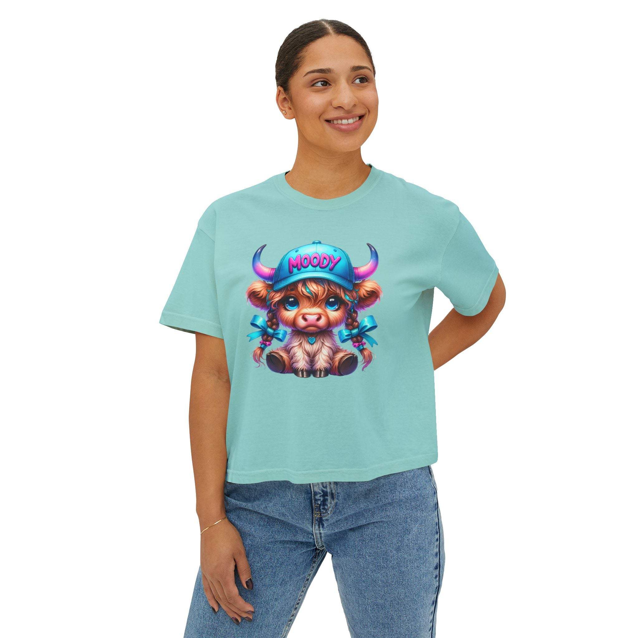 Woman wearing a boxy tee with a moody girl highland cow graphic on a light blue shirt