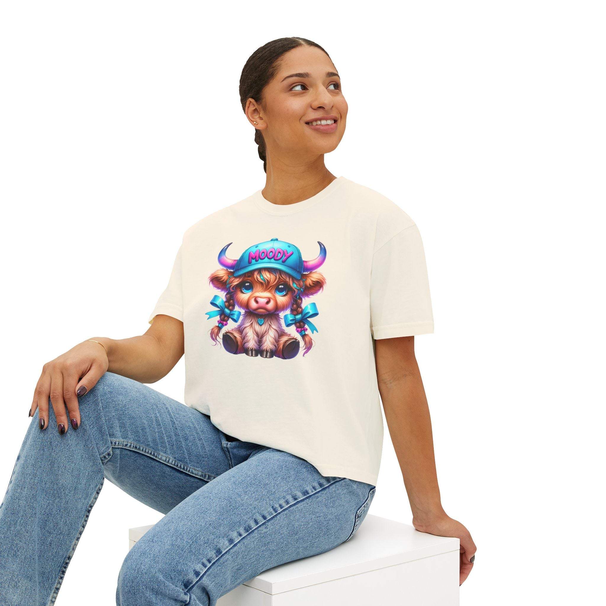 Woman wearing white boxy tee with moody girl highland cow graphic sitting and smiling
