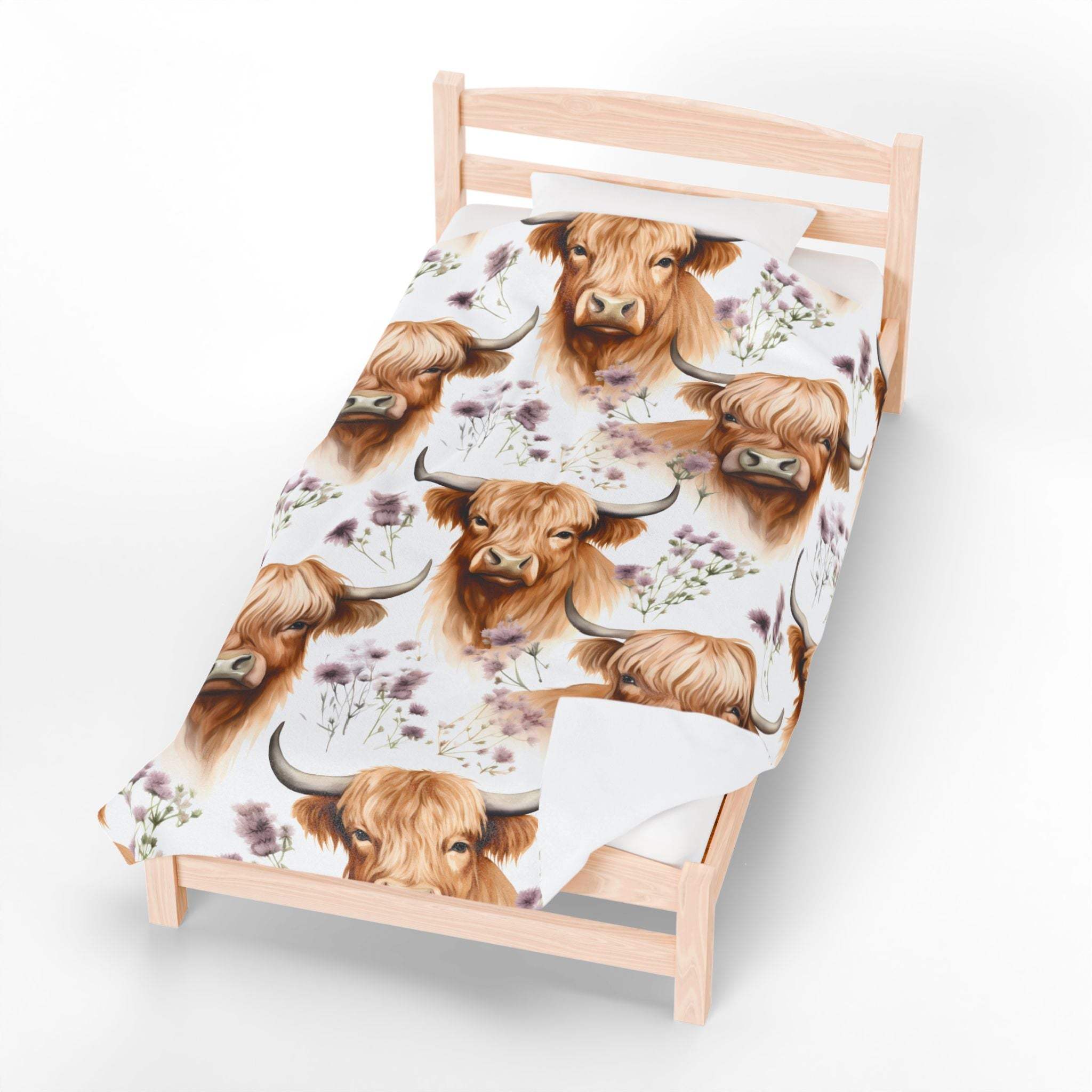 Plush blanket with floral highland cow design on wooden bed