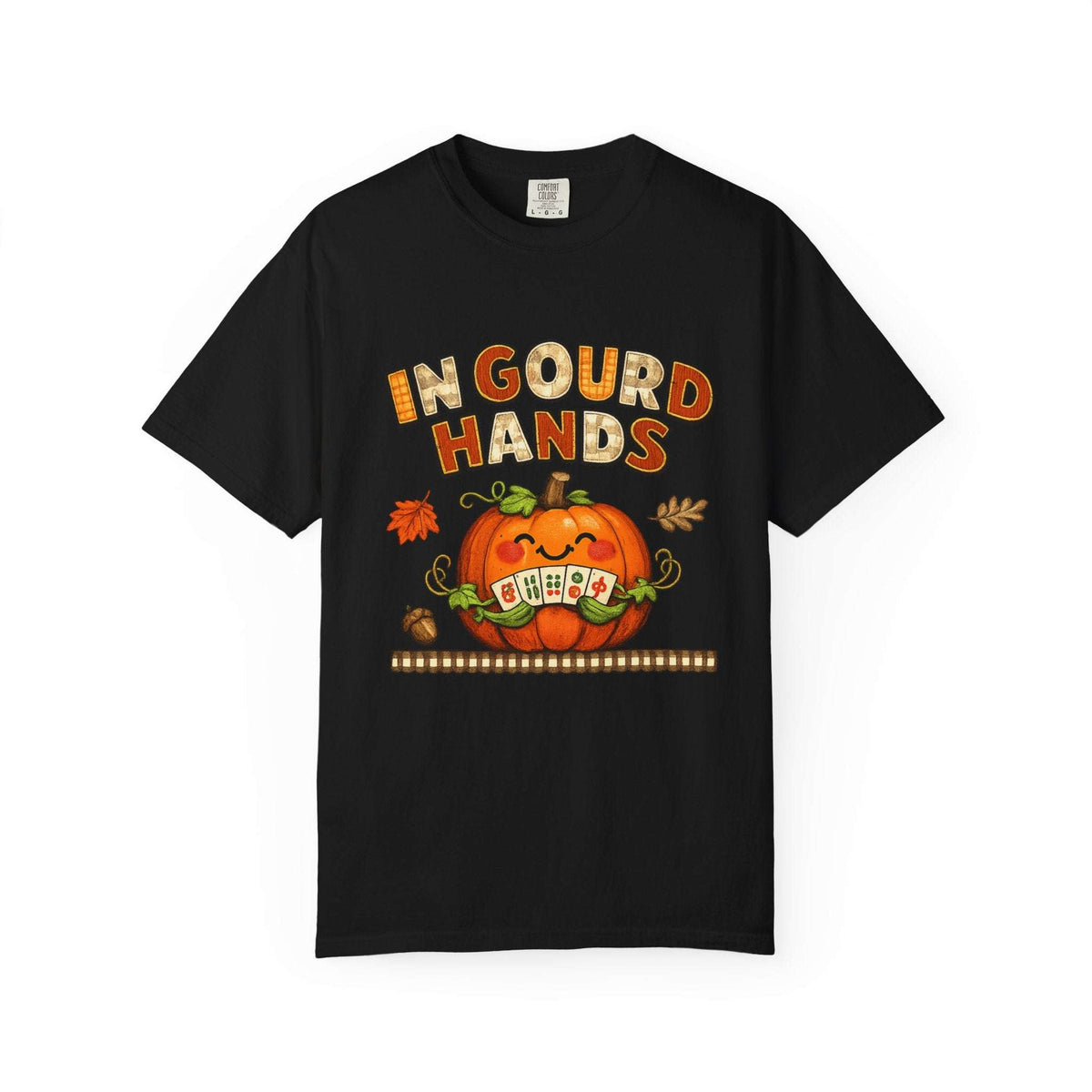 A black short-sleeve crewneck t-shirt featuring a festive Halloween graphic on the front. The graphic displays the phrase 'IN GOURD HANDS' in orange and yellow textured lettering above a smiling orange jack-o'-lantern pumpkin with a 'OH EA' sign in its mouth, accented with small orange and brown autumn leaves.