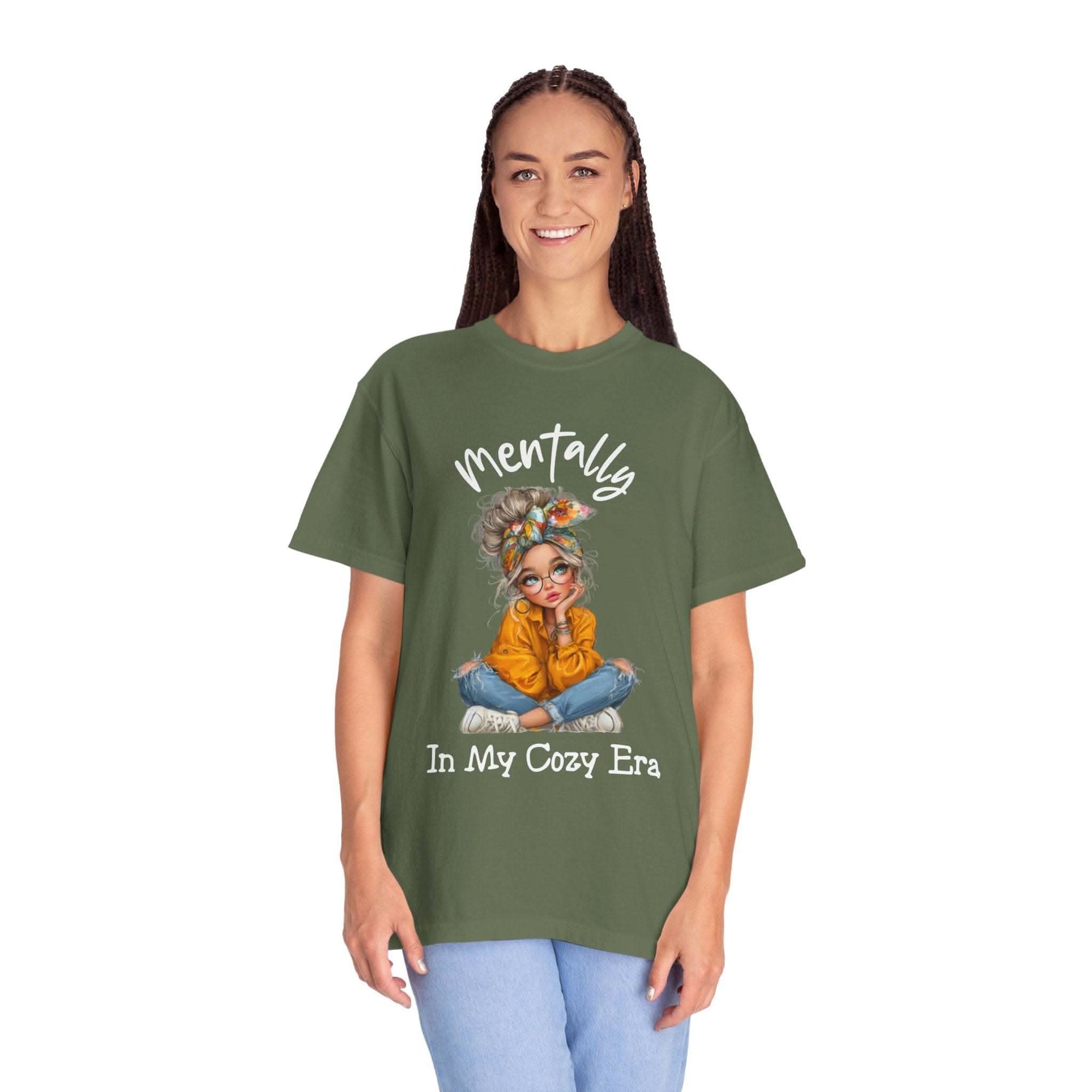 Woman wearing olive green Mentally in My Cozy Era t-shirt with graphic girl illustration and hand-lettered text.