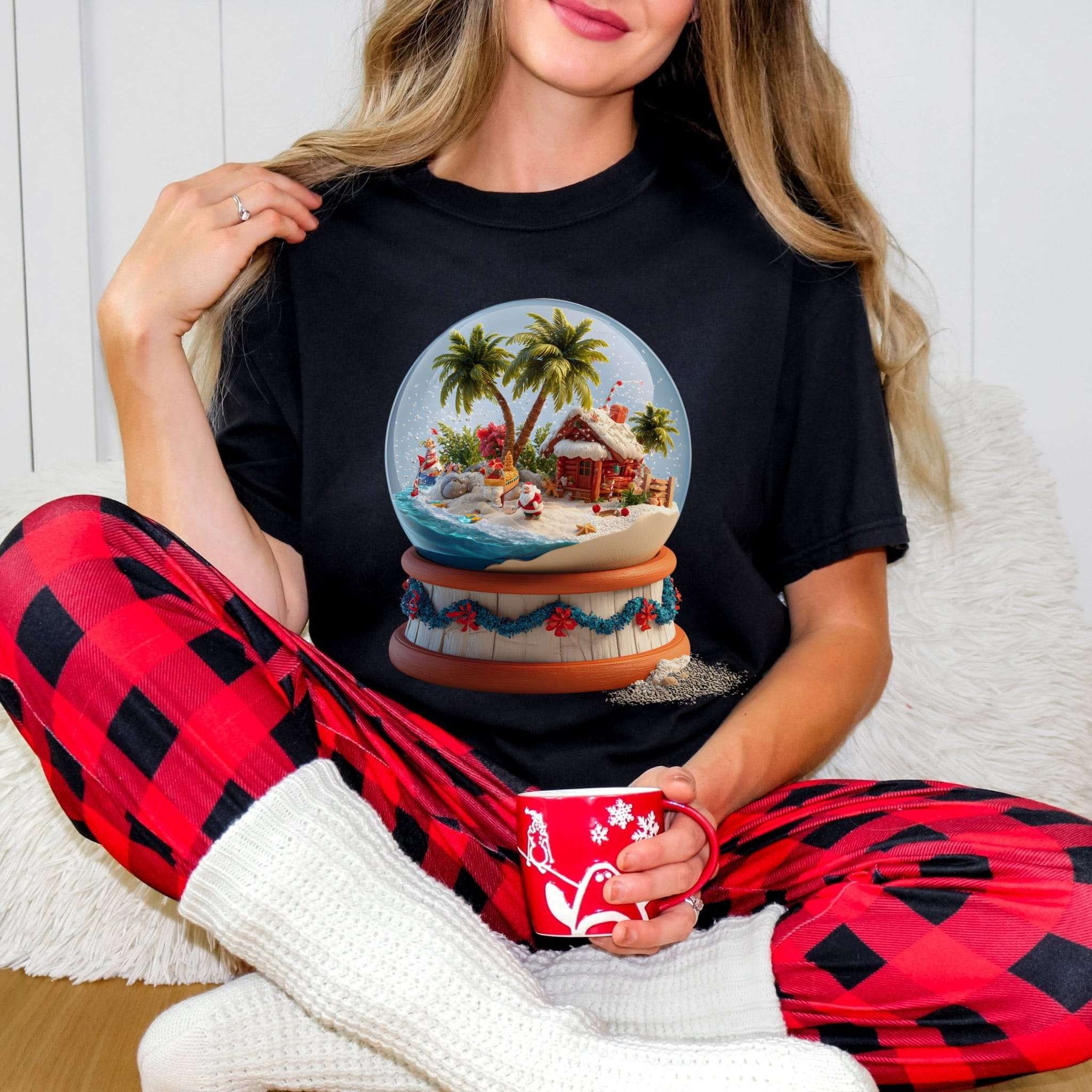 Woman wearing black Tropical Snow Globe T-shirt with palm tree snow globe design sitting in red plaid pants and white socks holding red mug