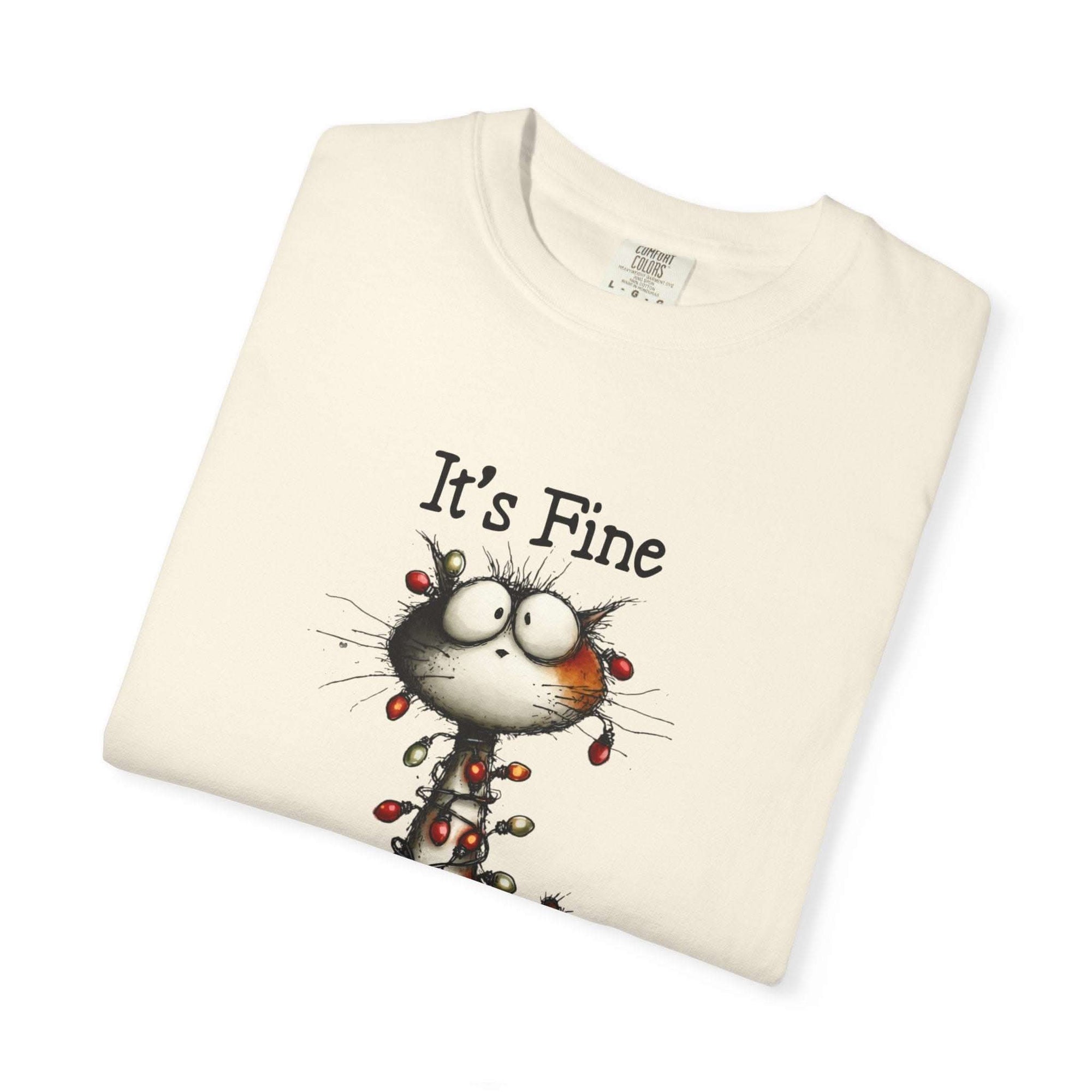 Folded cream-colored t-shirt with a cartoon cat and 'It's Fine' text on a white background