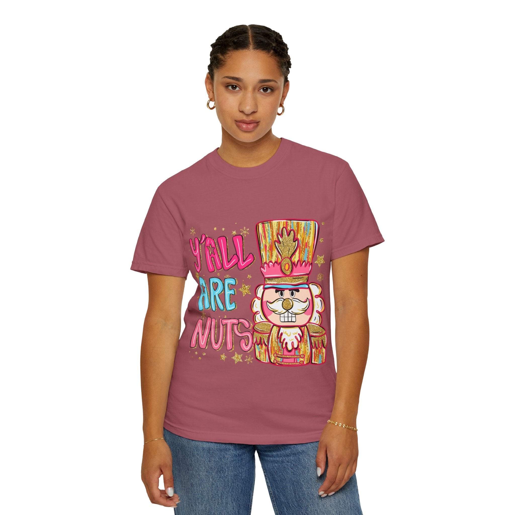 Woman wearing a Yall Are Nuts Nutcracker festive t-shirt in mauve with colorful nutcracker graphic and text