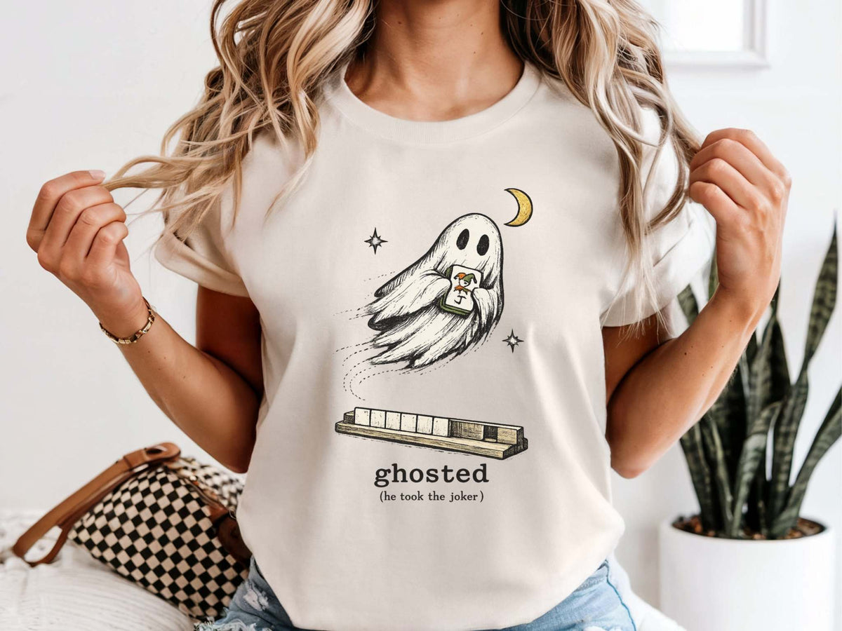 Model wearing an ivory mahjong T-shirt with a ghost holding a joker tile above a tile rack and “ghosted (he took the joker)” lettering.