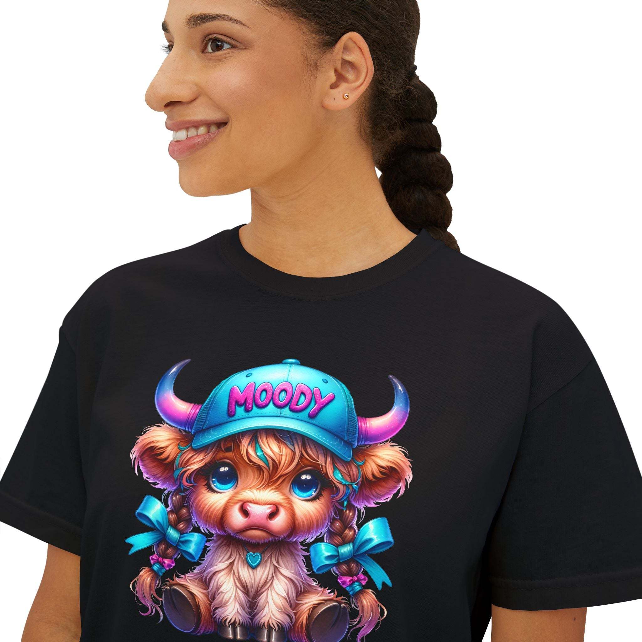Woman wearing black boxy tee with moody girl highland cow graphic and blue cap design