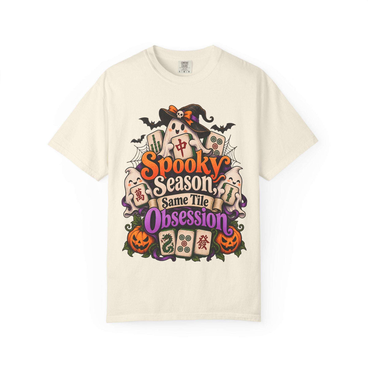 Flat lay of an ivory Halloween mahjong T-shirt with ghosts, pumpkins, mahjong tiles and “Spooky Season, Same Tile Obsession” lettering.
