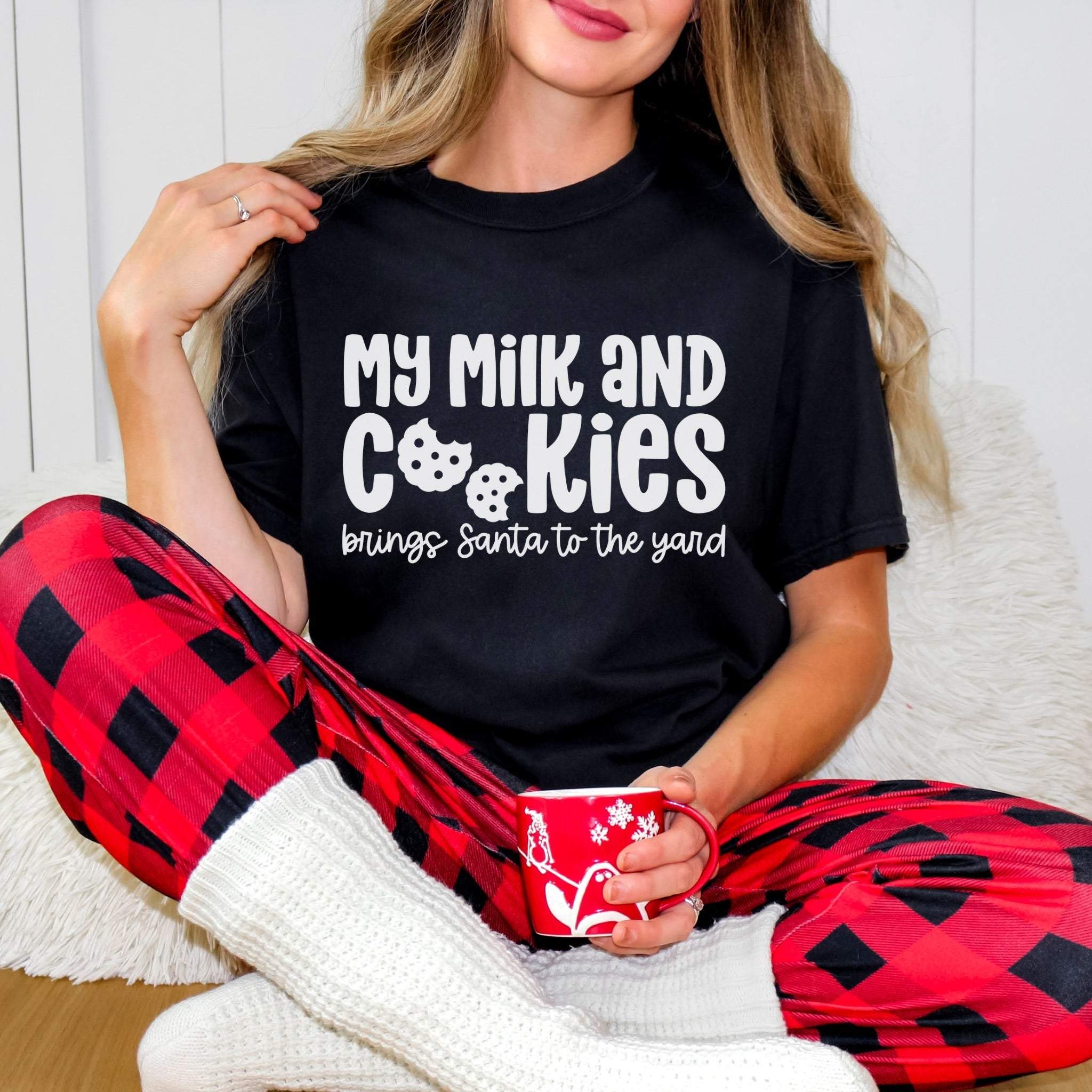 Woman wearing black My Milk and Cookies Christmas T-shirt with red plaid pants holding red mug