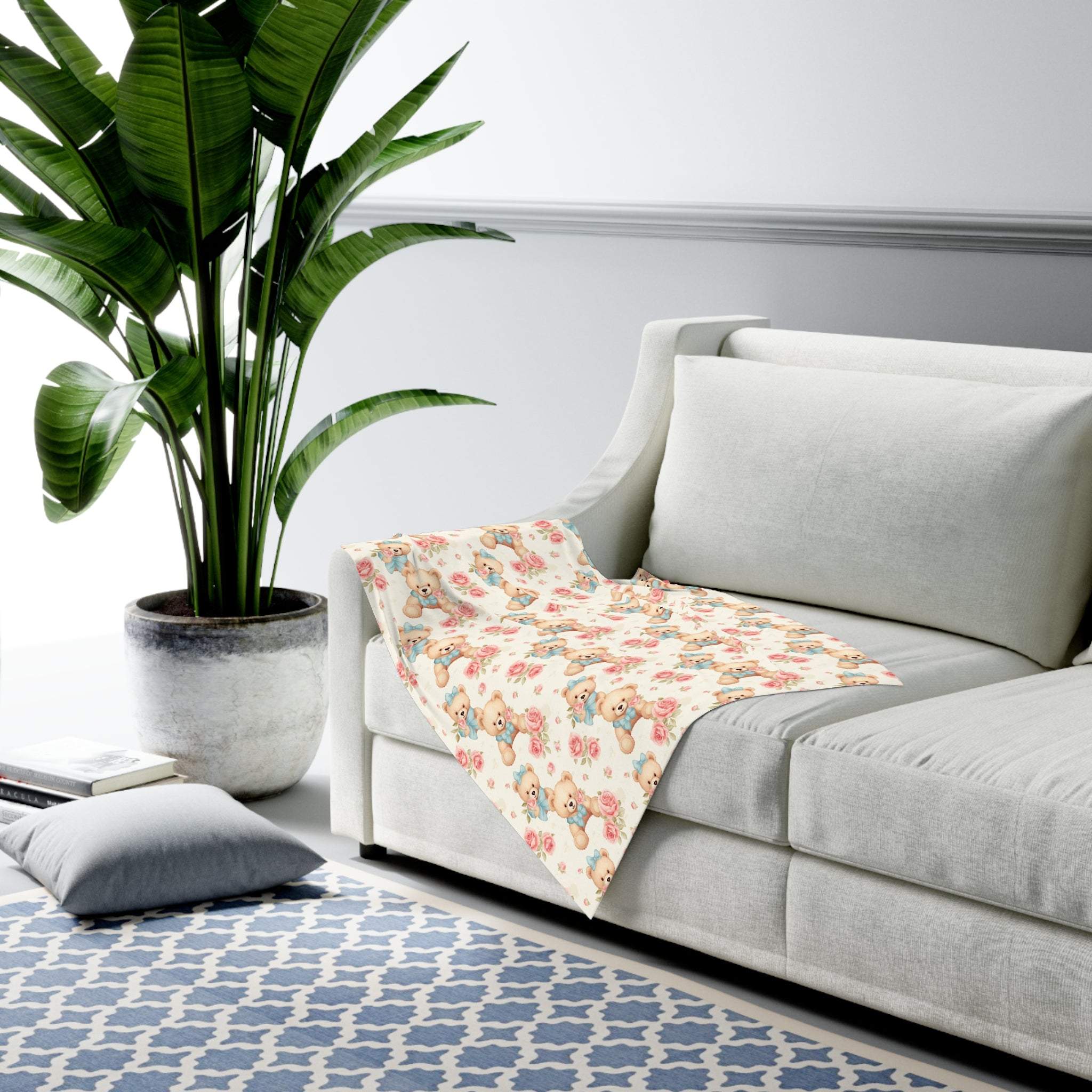 Floral teddy bear swaddle blanket on gray sofa in modern living room with plant and patterned rug