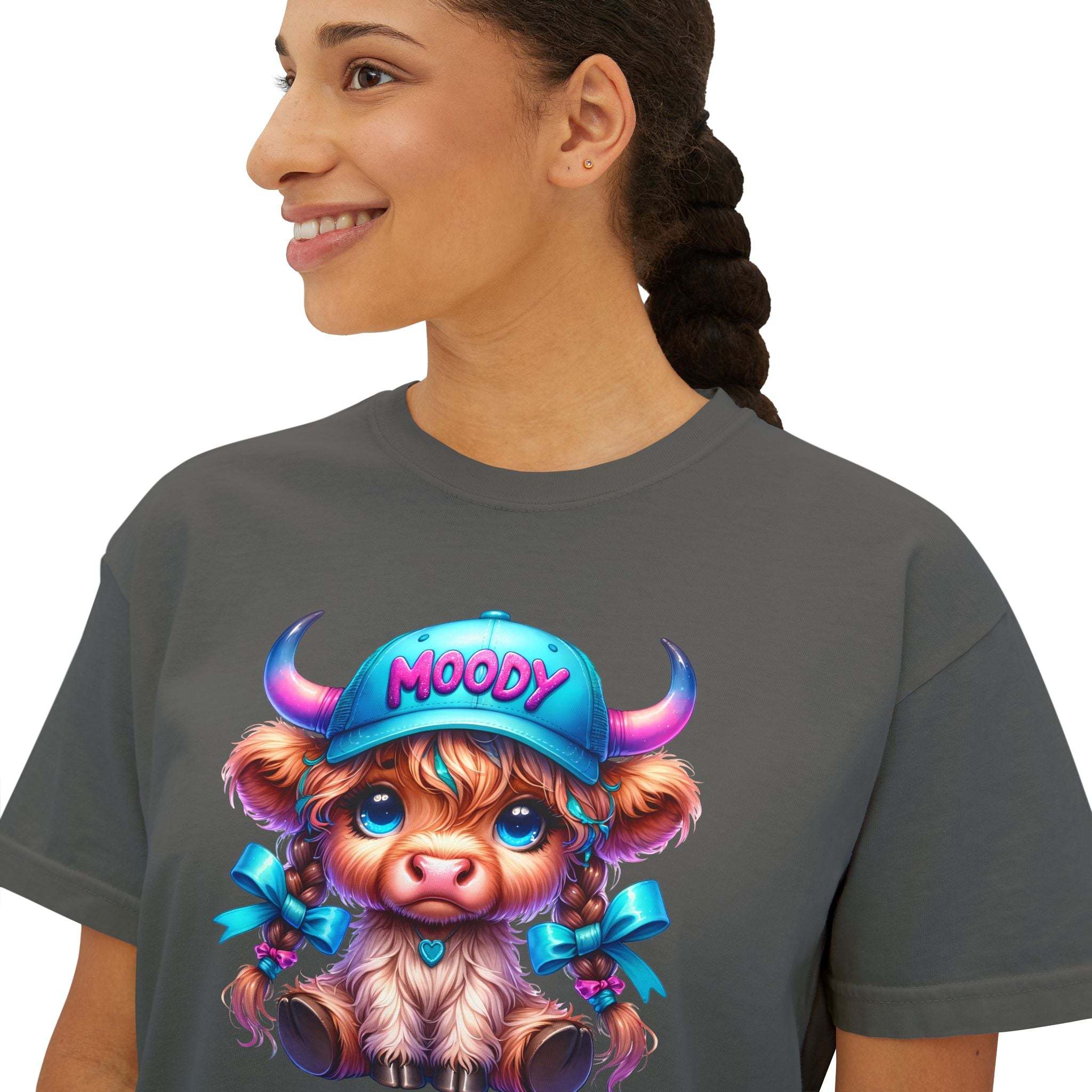 Woman wearing boxy tee with moody girl highland cow graphic and blue hat on front