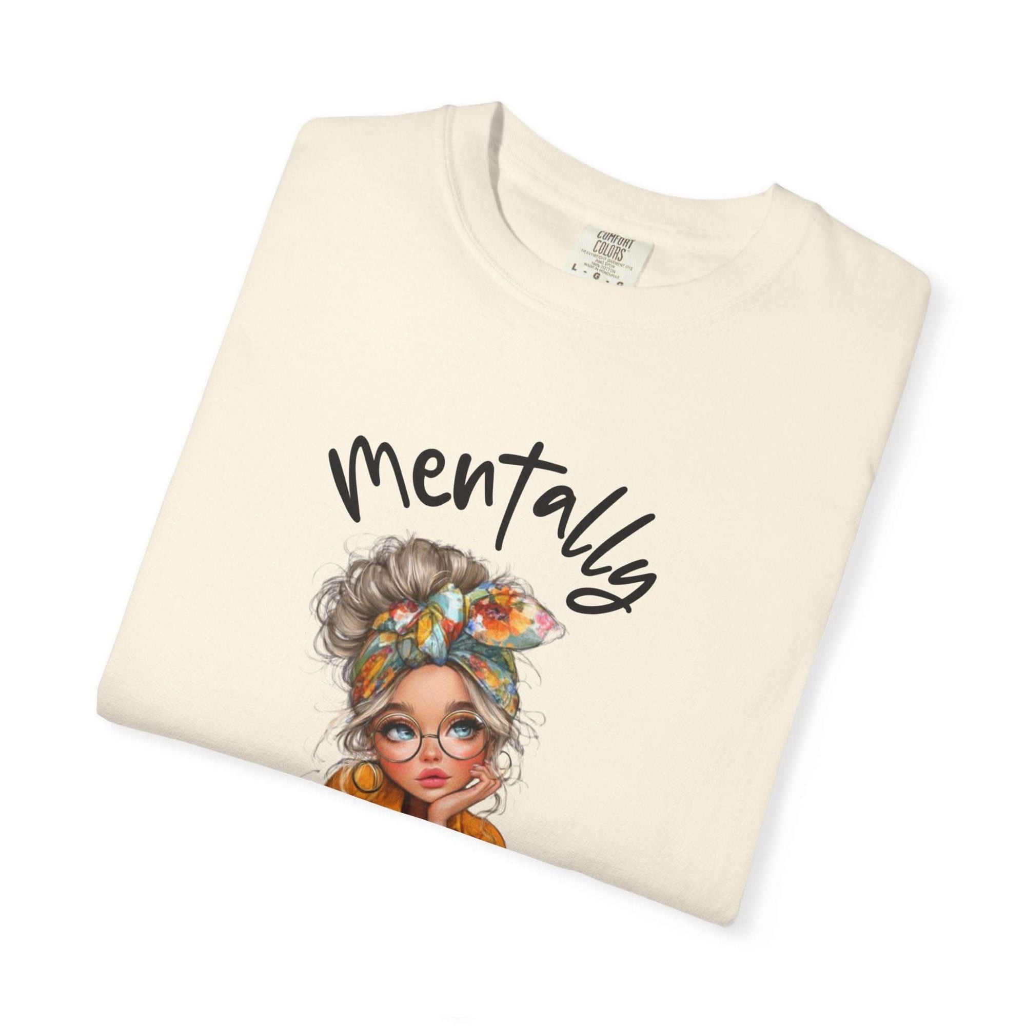 Folded cream-colored t-shirt with a graphic of a woman's head and 'mentally' text on a white background