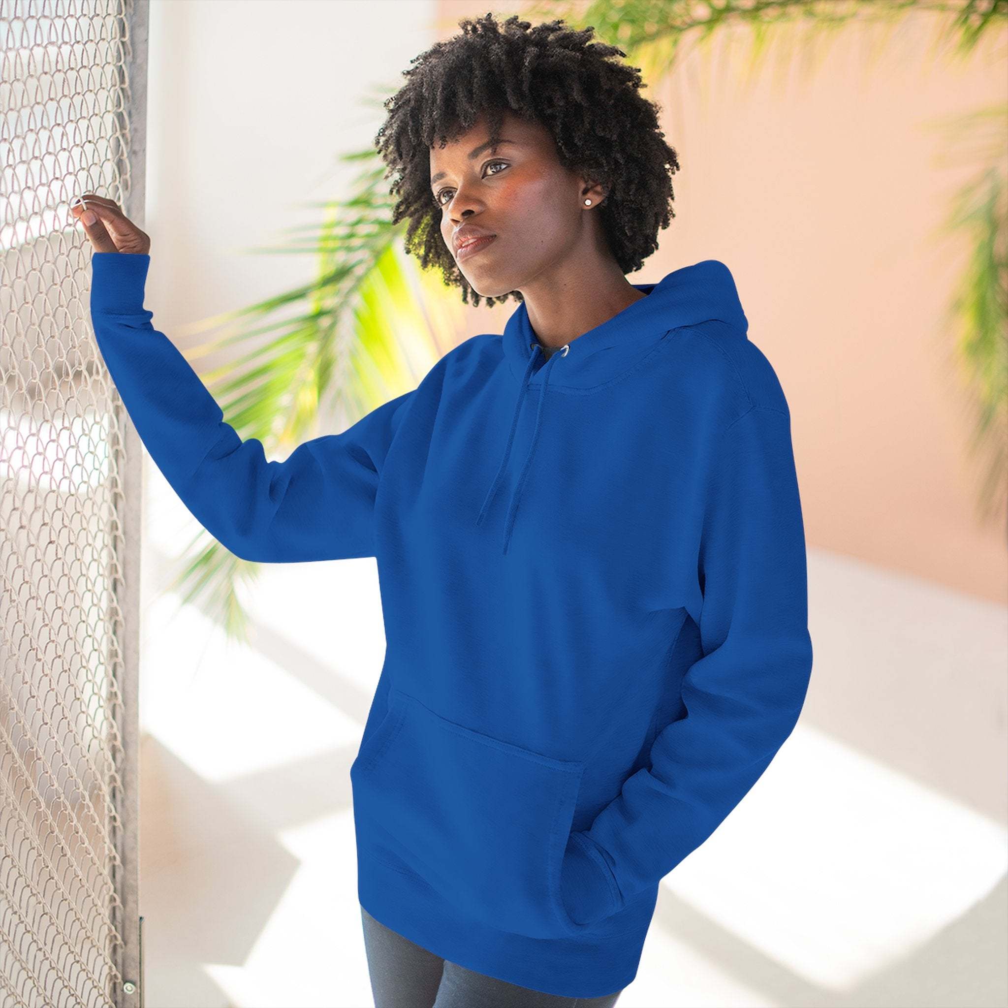 Woman wearing blue fleece hoodie with kangaroo pocket and adjustable hood standing indoors