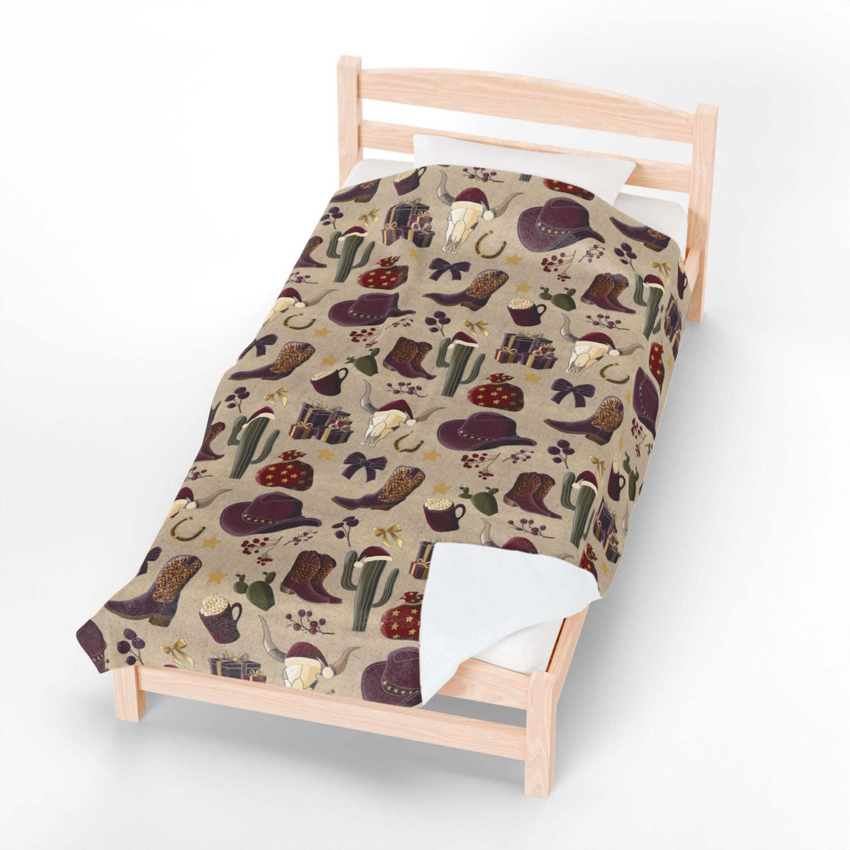 Plush blanket with cowboy Christmas design featuring boots, hats, cacti, and festive elements on bed