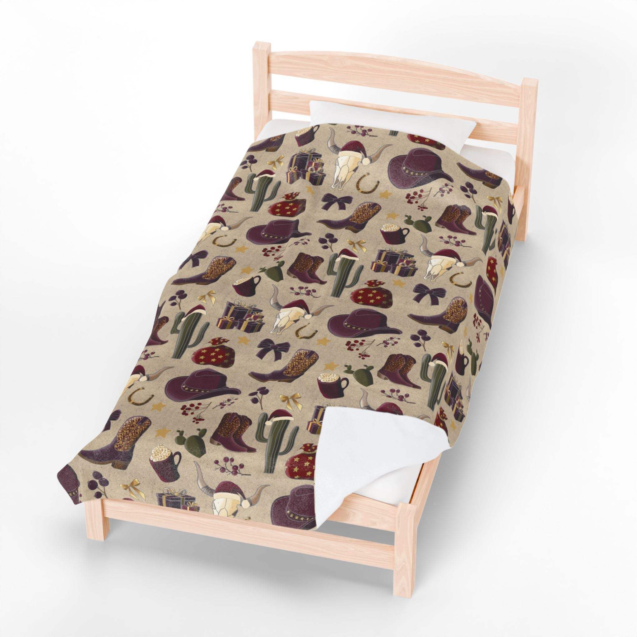 Plush blanket with cowboy Christmas design featuring boots, hats, cacti, and festive elements on bed