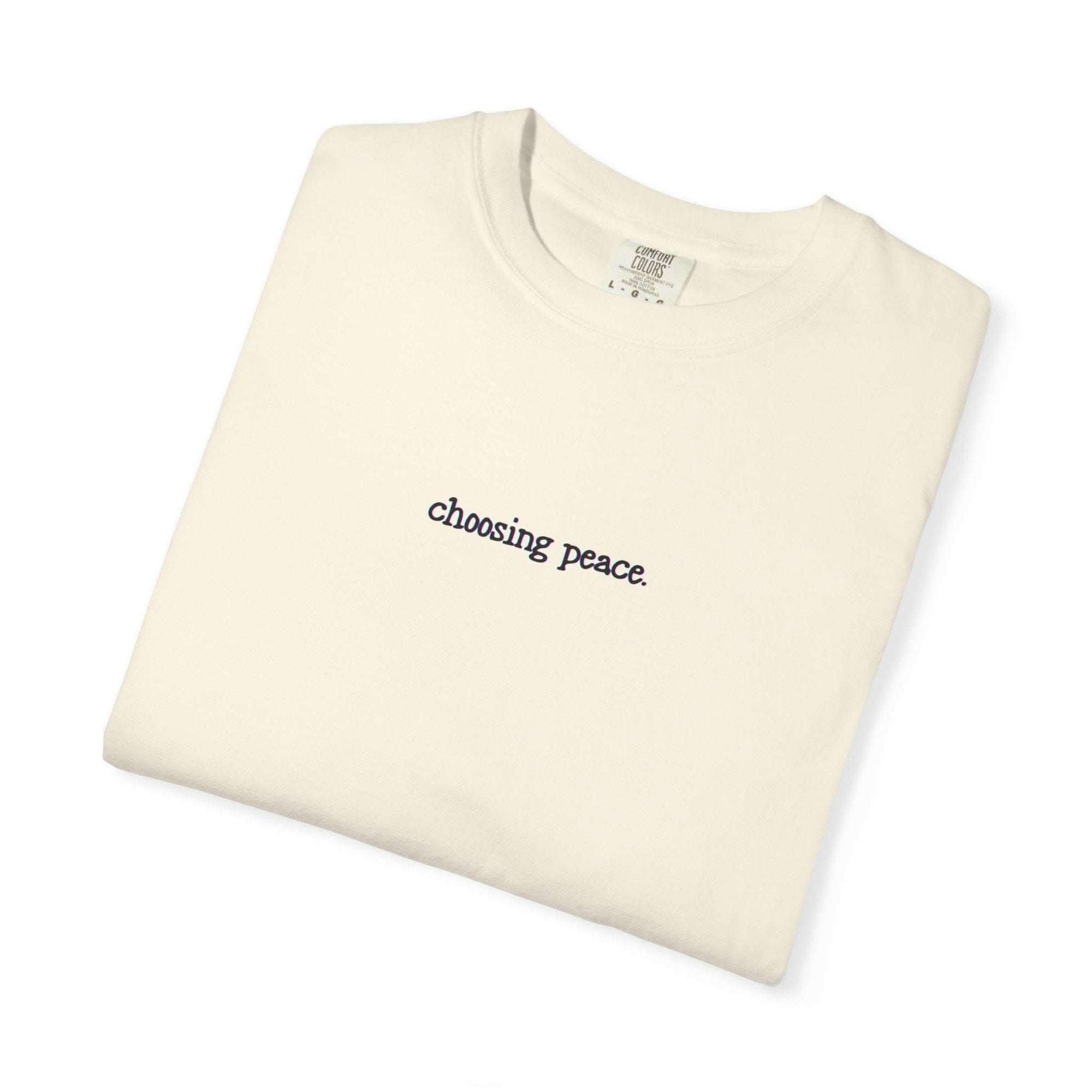Folded cream-colored t-shirt with 'choosing peace' text on a white background