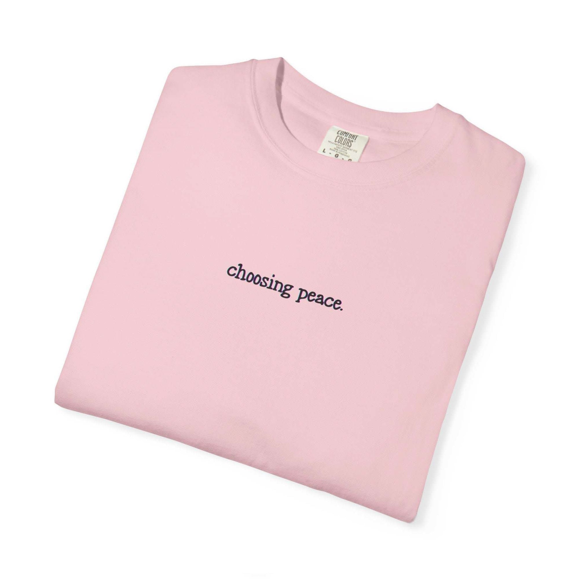 Folded pink t-shirt with 'choosing peace' text on a white background