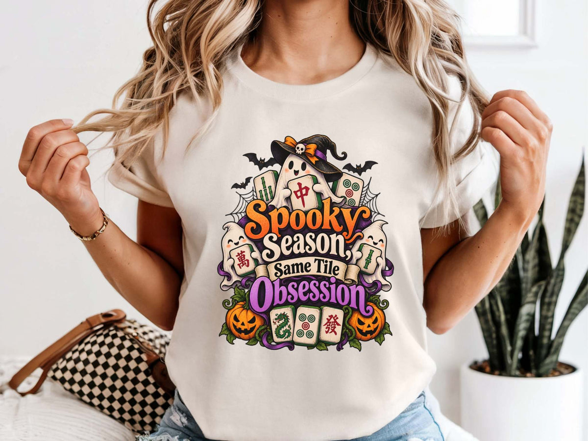 Model wearing an ivory Halloween mahjong T-shirt with ghosts, pumpkins, mahjong tiles and “Spooky Season, Same Tile Obsession” lettering.