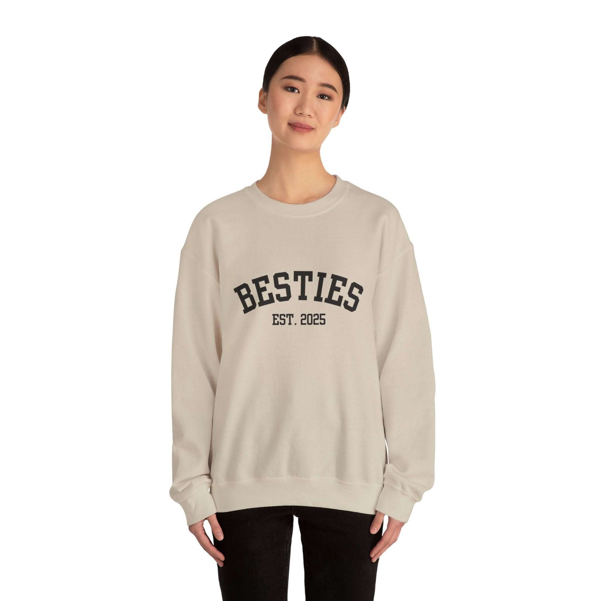Person wearing a beige sweatshirt with 'BESTIES EST. 2025' text on a white background