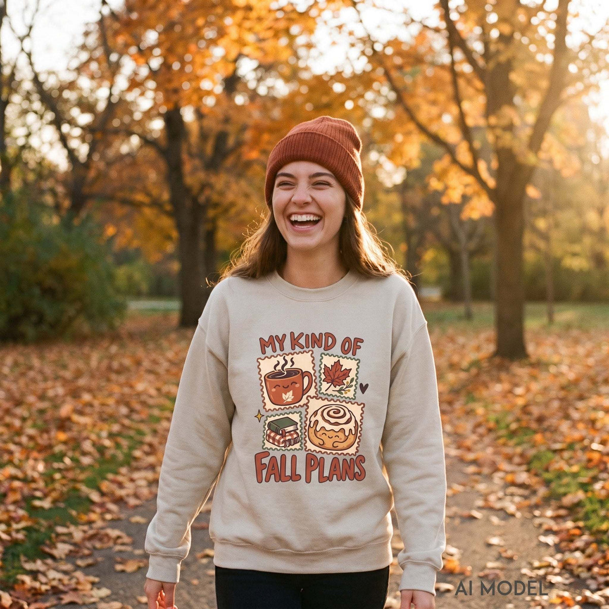 Woman wearing a sand My Kind of Fall Plans crewneck sweatshirt and rust knit beanie, showing the autumn graphic against golden park foliage.