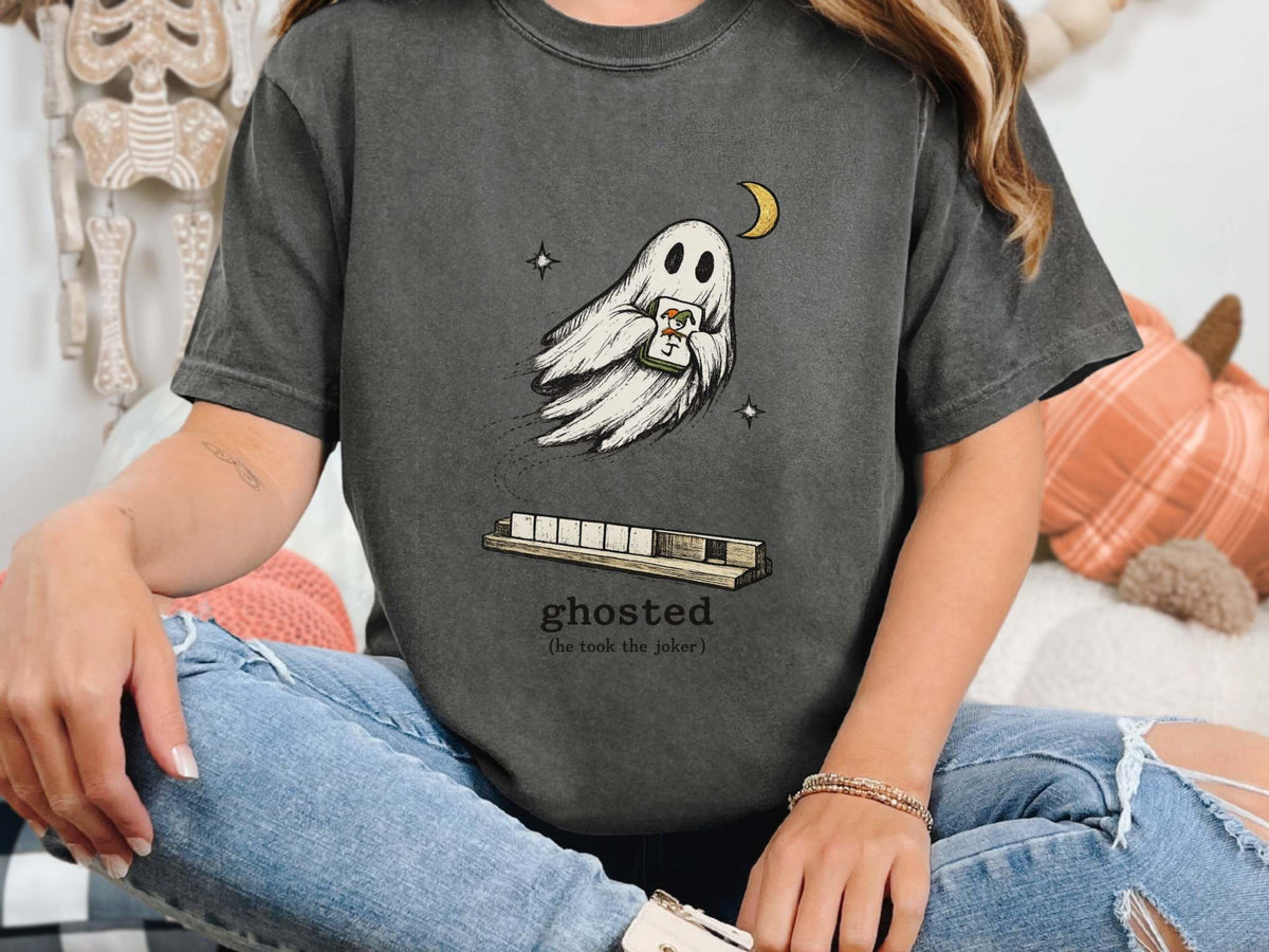 Model wearing a pepper mahjong T-shirt with a ghost holding a joker tile above a tile rack and “ghosted (he took the joker)” lettering.