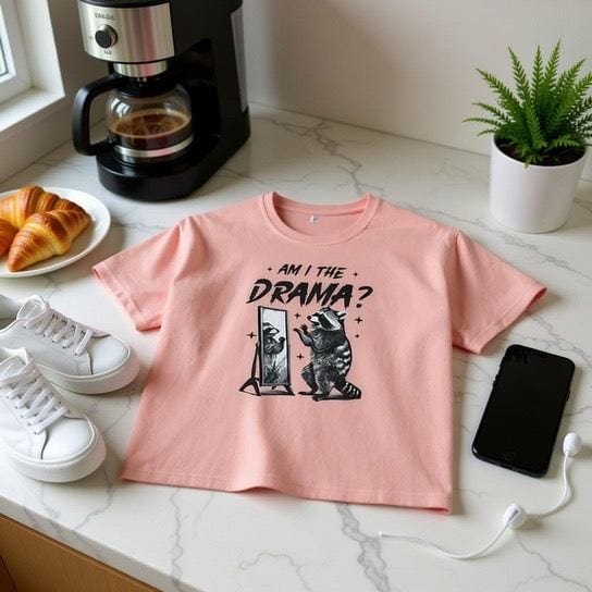 Pink boxy tee with "Am I The Drama?" raccoon graphic and vintage pigment dye look