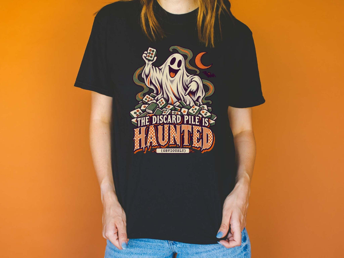Model wearing black Comfort Colors 1717 Halloween mahjong T-shirt with a ghost holding a tile and “The Discard Pile Is Haunted (Obviously)” lettering.