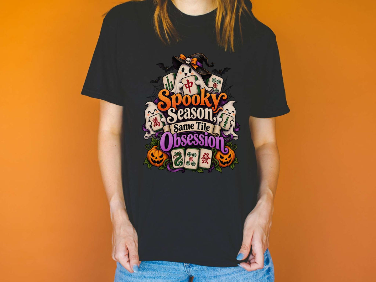 Model wearing a black Halloween mahjong T-shirt with ghosts, pumpkins, mahjong tiles and “Spooky Season, Same Tile Obsession” lettering.
