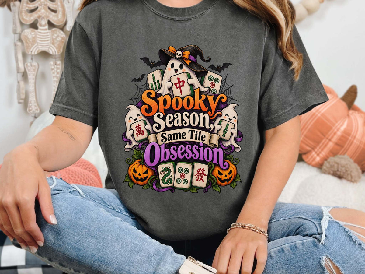 Model wearing a pepper Halloween mahjong T-shirt with ghosts, pumpkins, mahjong tiles and “Spooky Season, Same Tile Obsession” lettering.