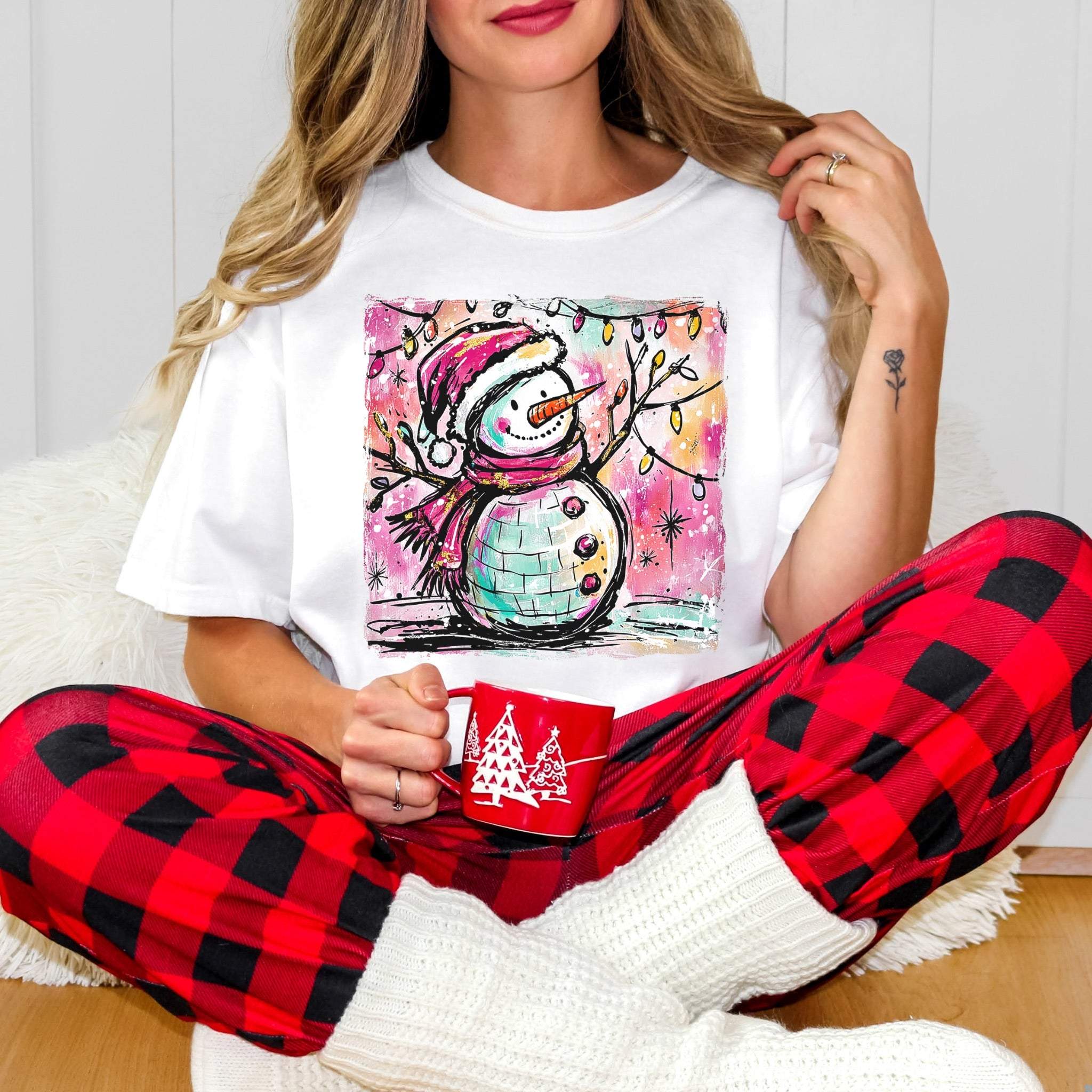 Woman wearing Retro Disco Ball Snowman T-shirt with red plaid pants and white socks holding a red holiday mug