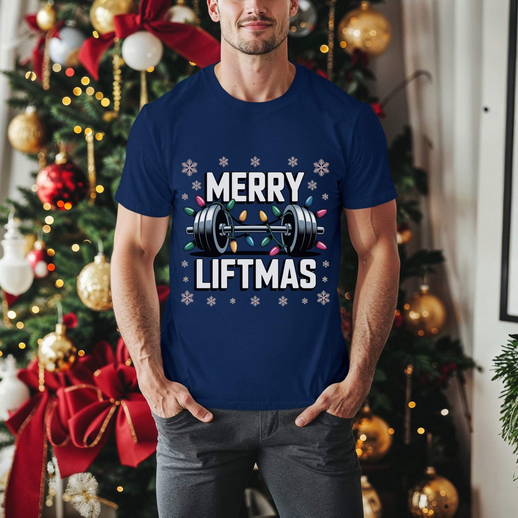 Man wearing navy Merry Liftmas Christmas workout t-shirt with barbell and holiday lights design standing in front of decorated Christmas tree