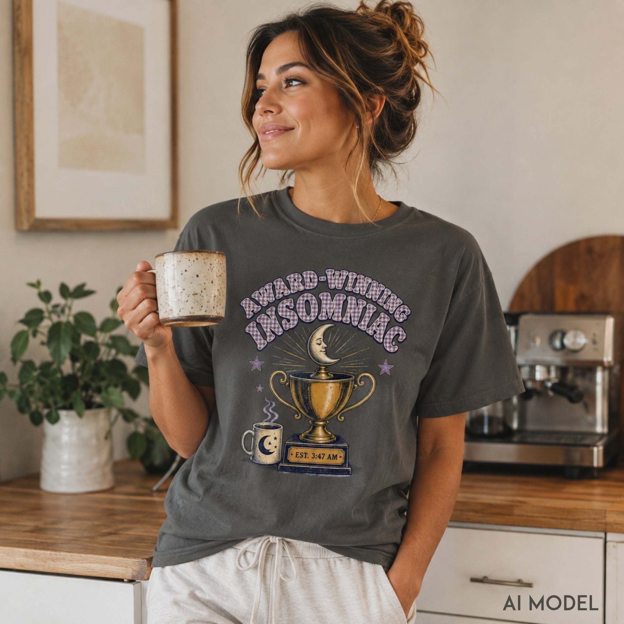 Female model wearing a pepper gray Award-Winning Insomniac T-shirt with vintage moon, trophy and coffee graphic in a cozy kitchen setting.
