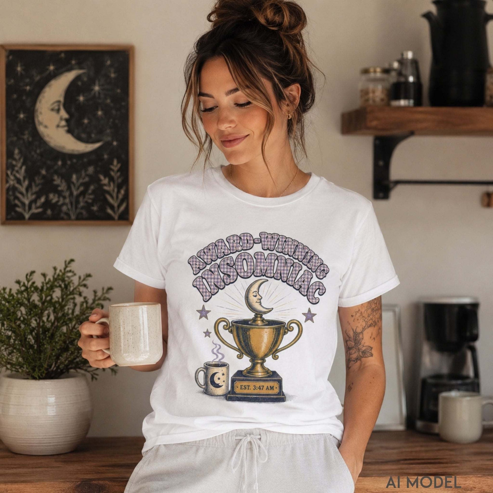 Female model wearing a white Award-Winning Insomniac graphic T-shirt featuring a crescent moon, trophy and coffee design while holding a mug.