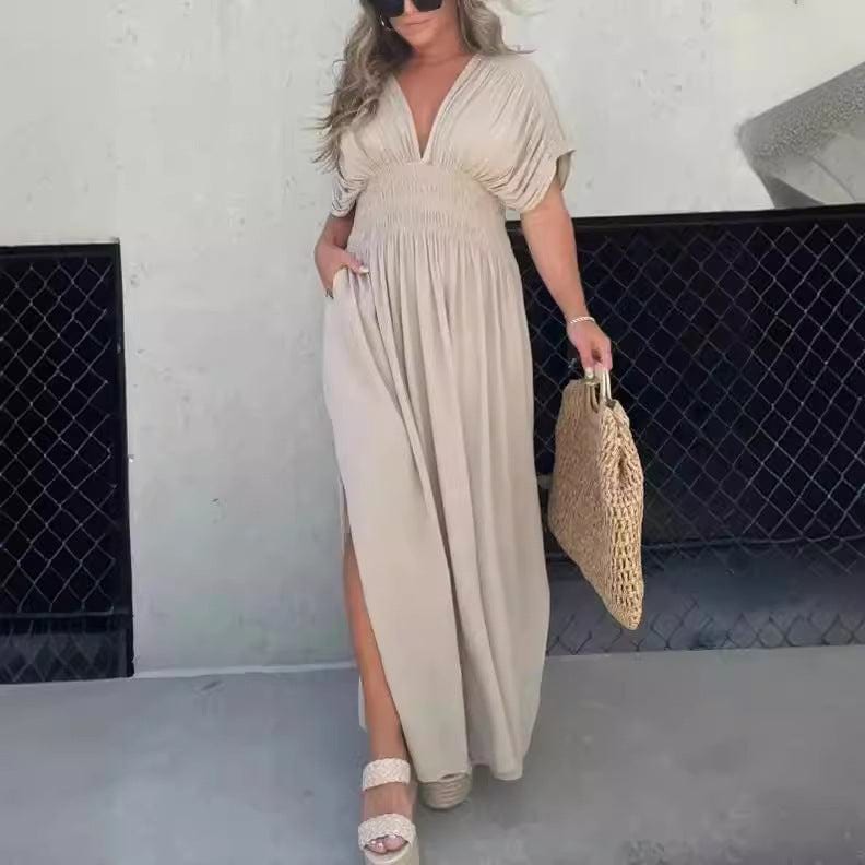 Woman wearing beige bat-sleeved V-neck summer dress with elastic waist and side slit holding a woven handbag