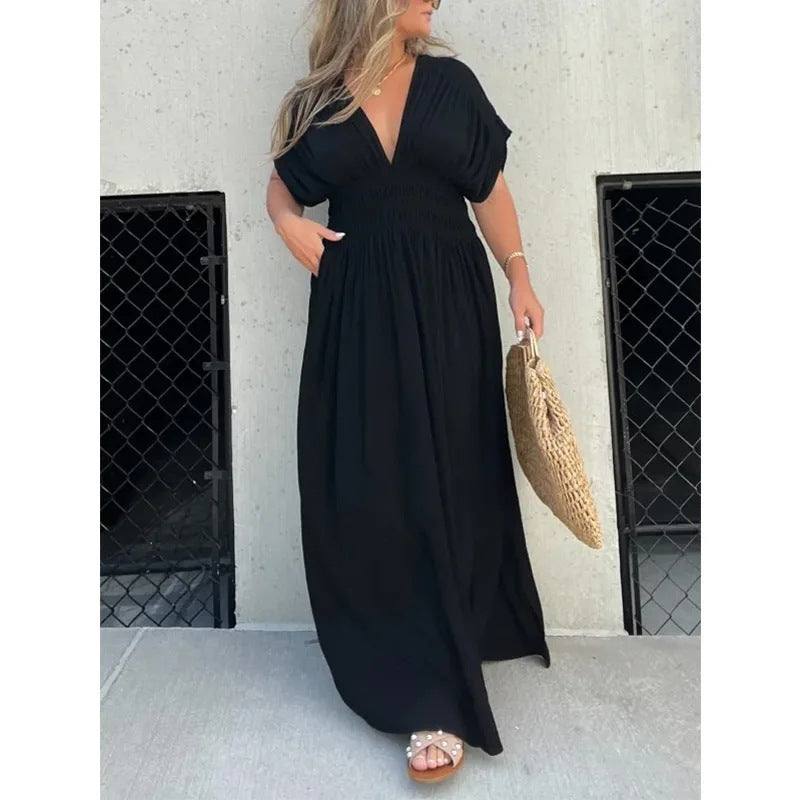 Woman wearing black bat-sleeved V-neck long summer dress with elastic waist and side slit holding woven bag