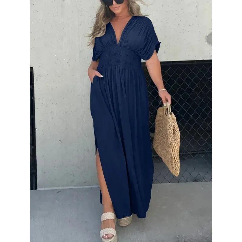 Woman wearing navy blue bat-sleeved V-neck slit summer dress with elastic waist and short sleeves, holding woven bag and wearing sandals.