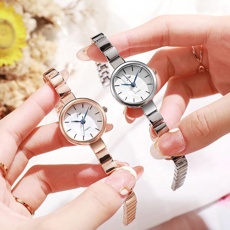 Two women's niche steel watches with simple round white dials and alloy metal straps in gold and silver colors held in hands against a blurred background