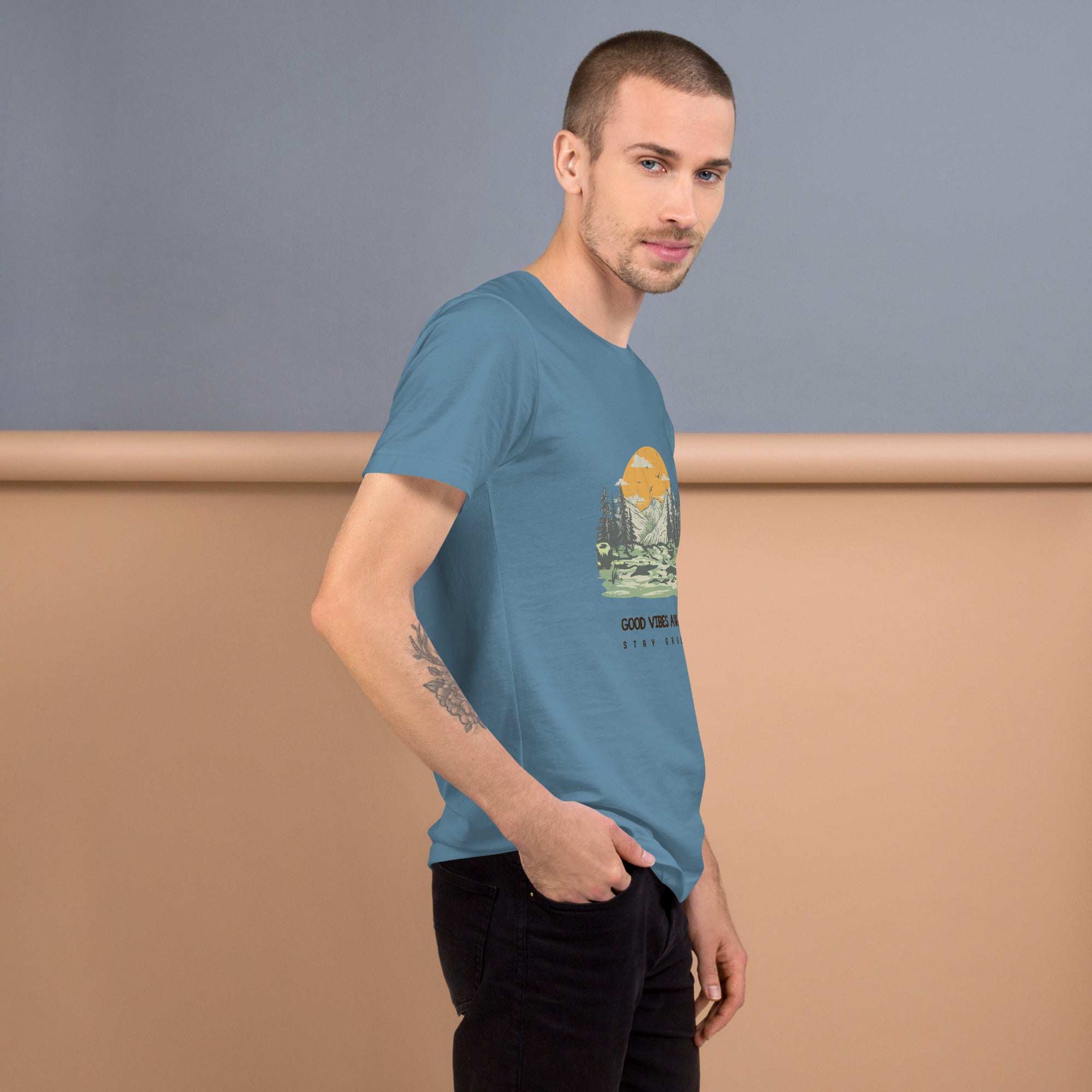 Man wearing blue Good Vibes T-Shirt with nature graphic standing against two-tone background