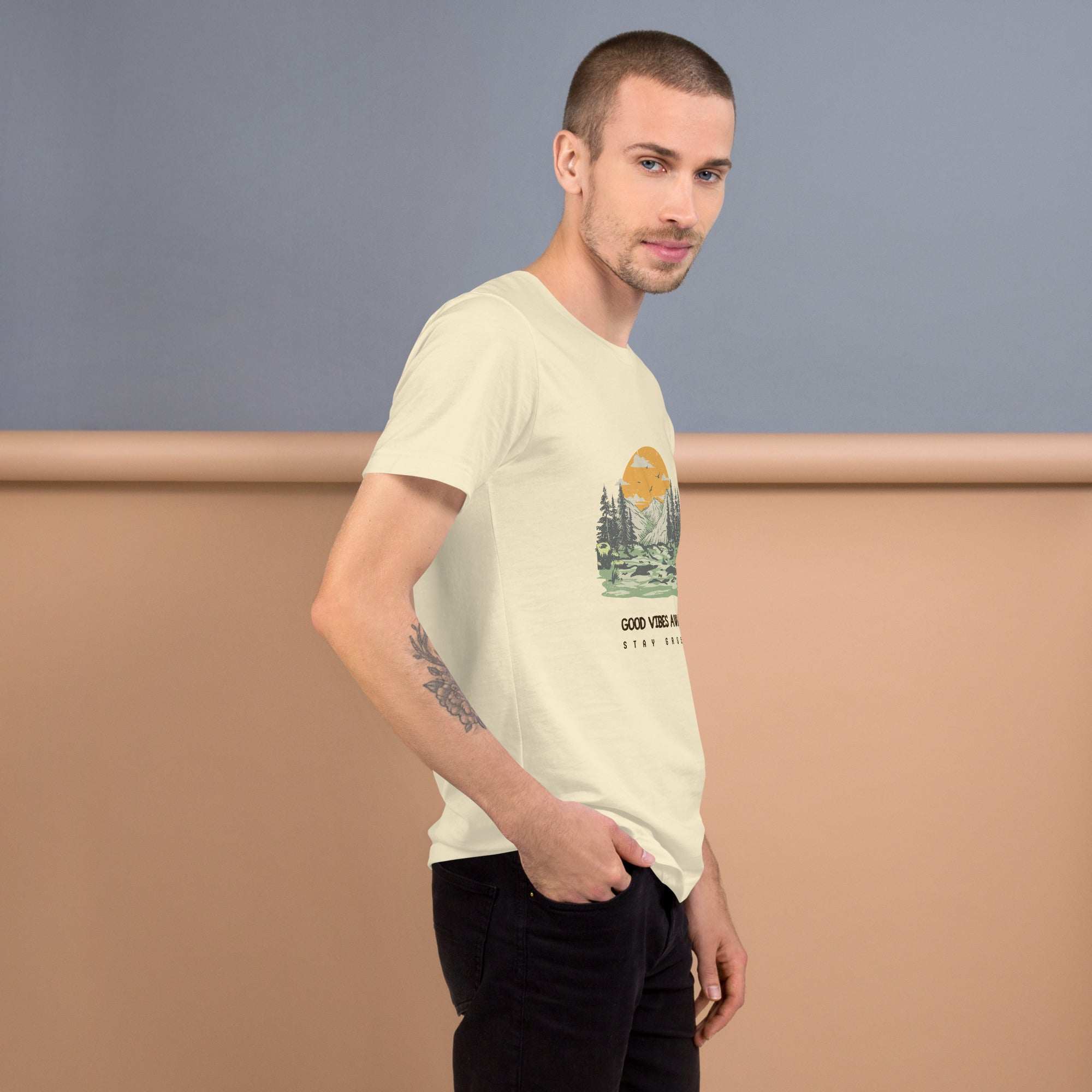 Man wearing light-colored Good Vibes T-Shirt with nature graphic and black pants against muted background