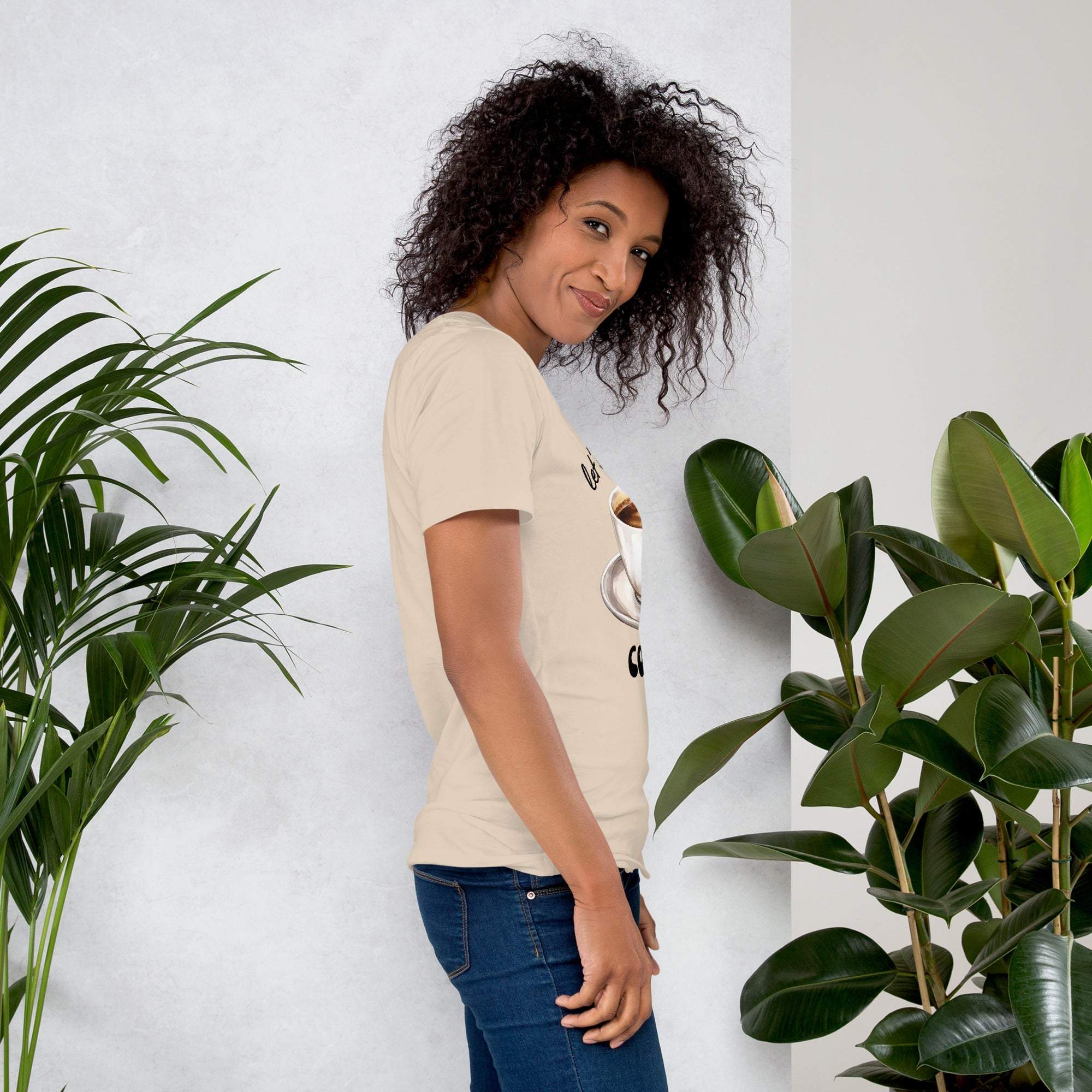 Woman wearing beige coffee t-shirt with coffee cup design standing near green plants