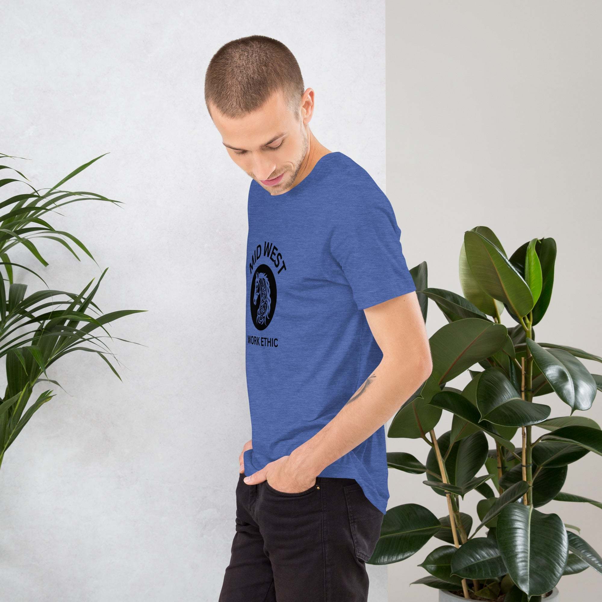 Man wearing blue Midwest T-Shirt with horse graphic and work ethic text standing beside plants