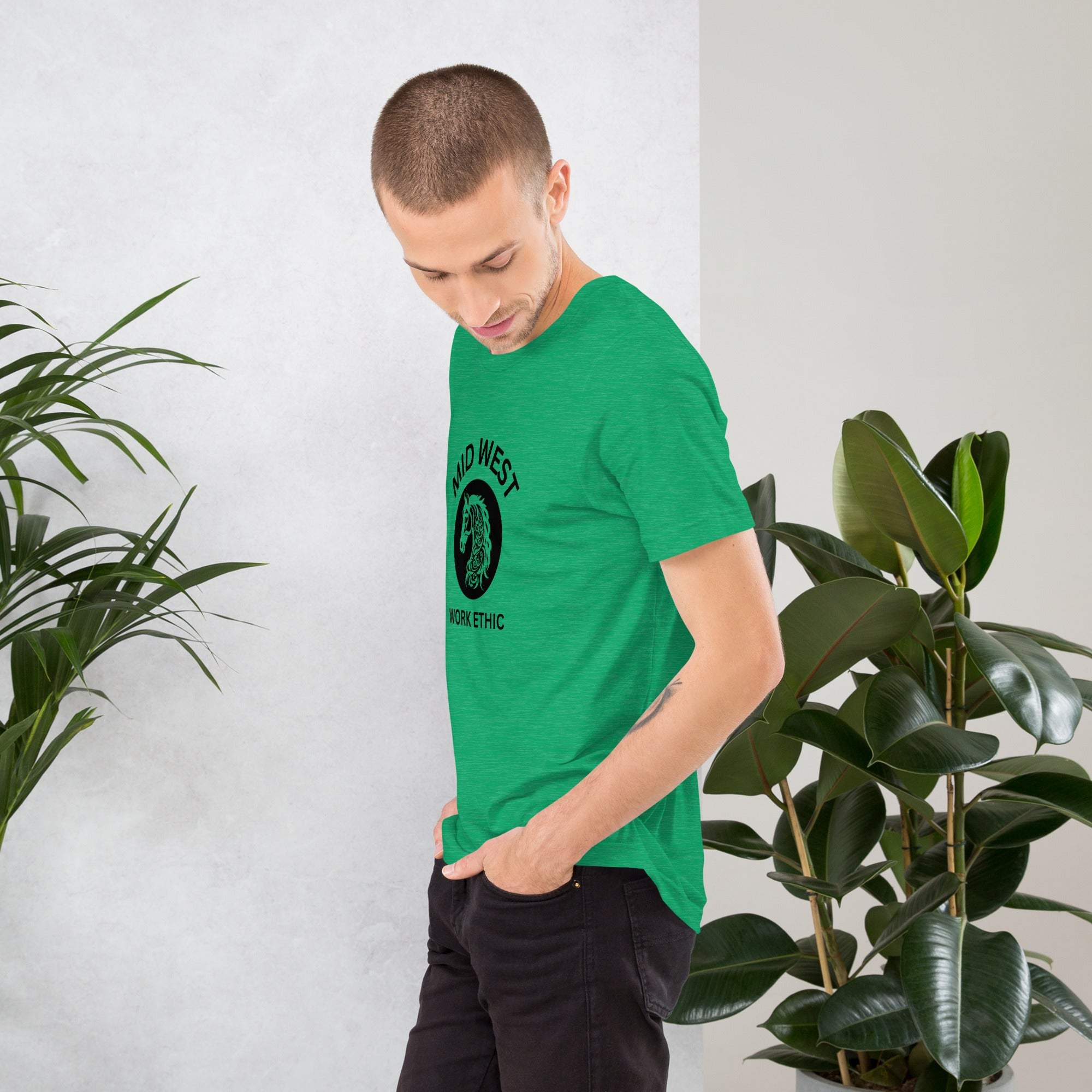 Man wearing green Midwest T-Shirt with horse graphic standing near plants in casual setting