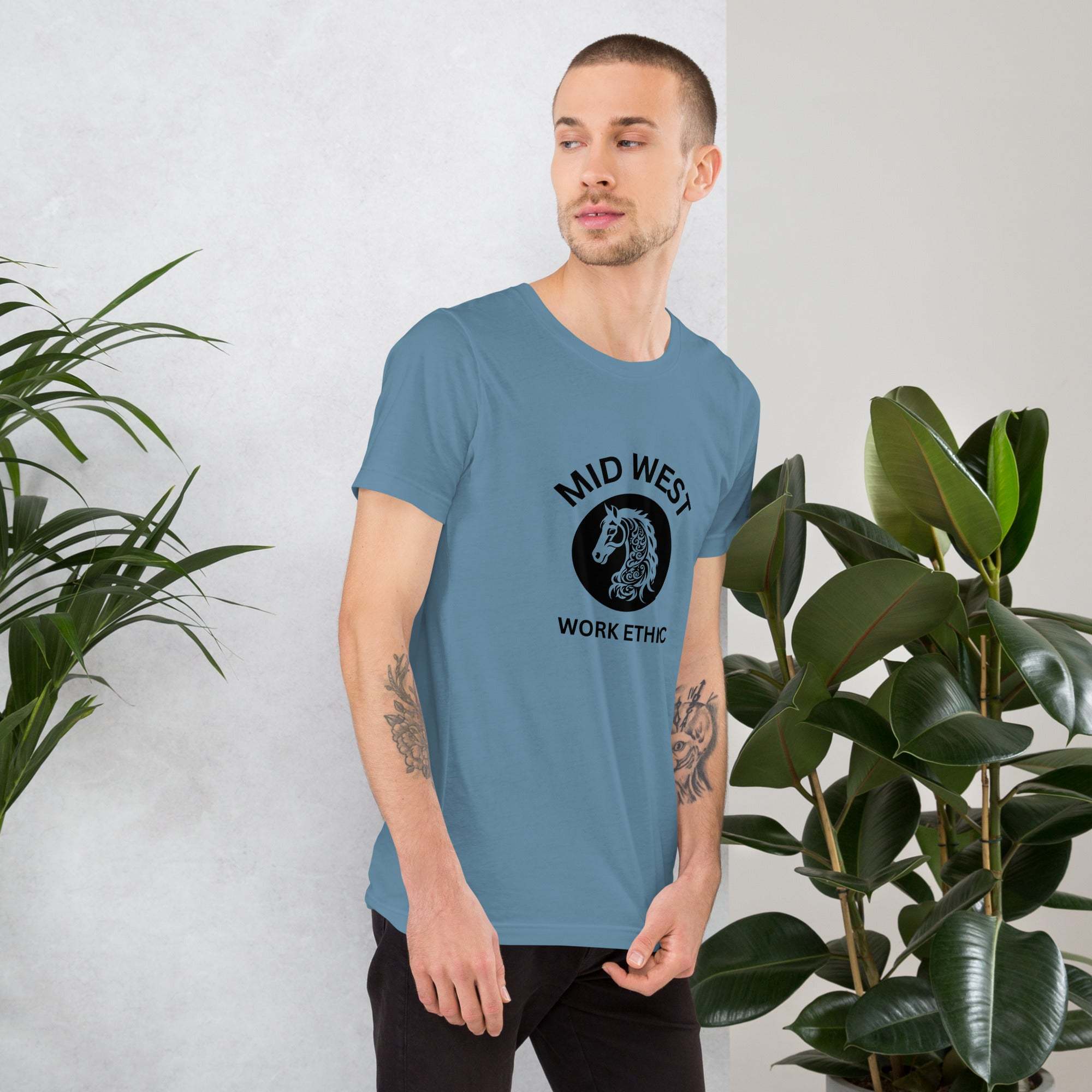 Man wearing blue Midwest work ethic T-shirt with horse graphic standing beside green plants